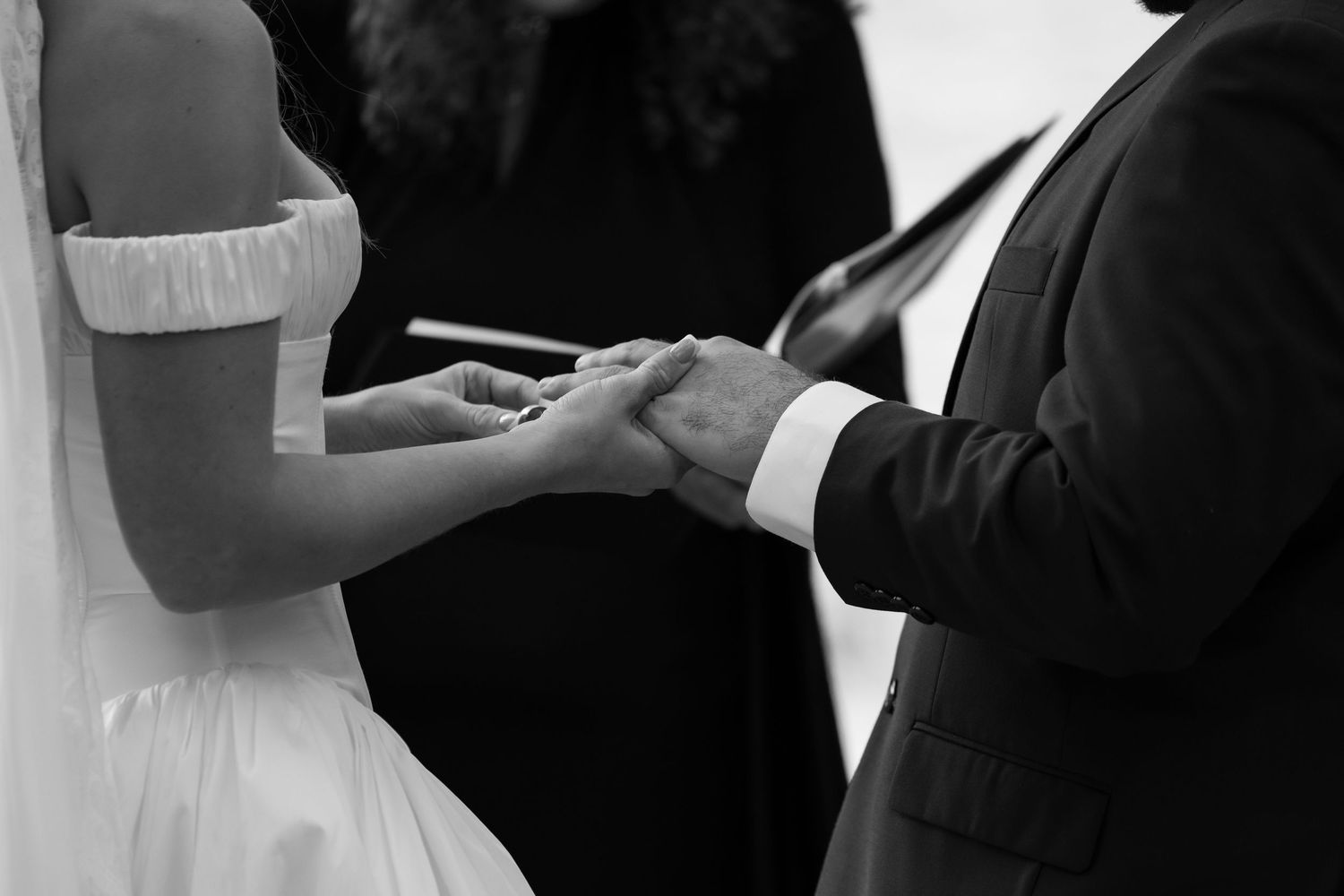 Black and white photo of bride and groom holding hands during wedding ceremony vows.