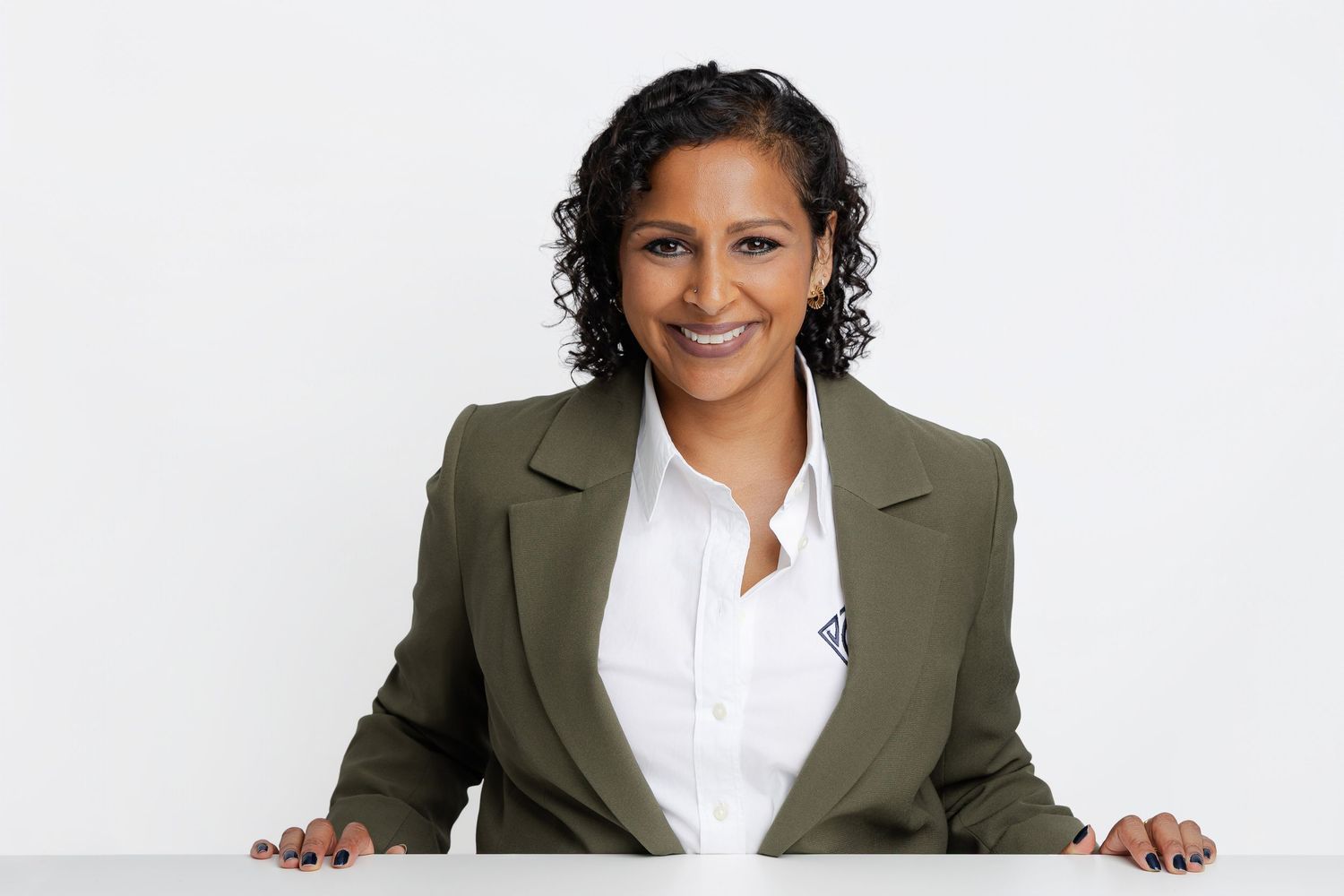 Professional woman in olive blazer smiling confidently at camera against white background.