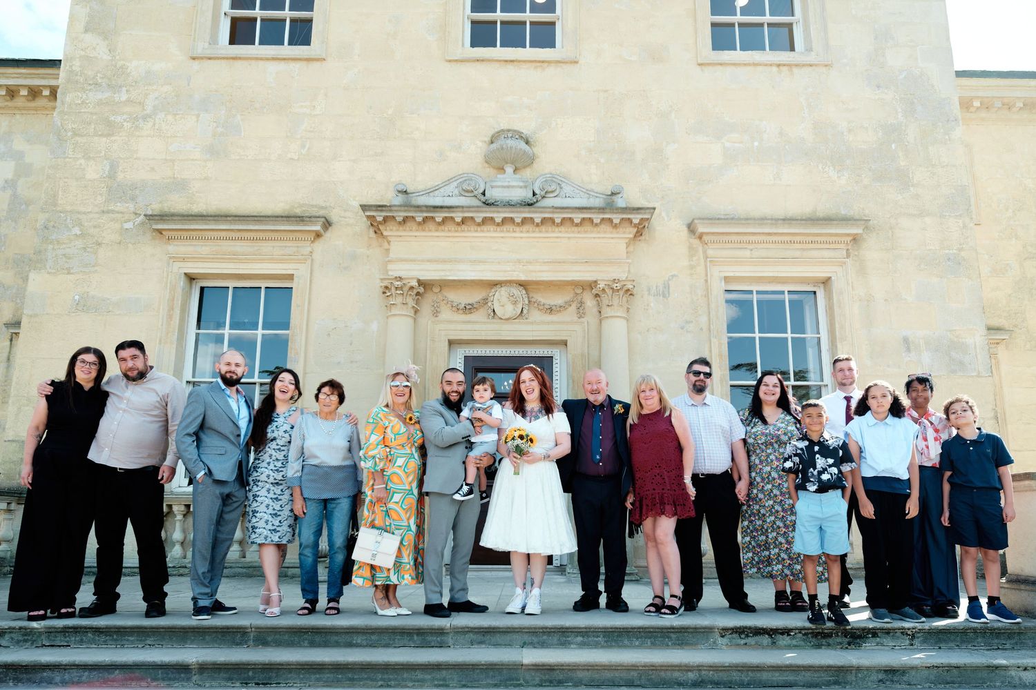 Wedding group photo with bride and groom surrounded by guests on steps of Danson House in Bexleyheath