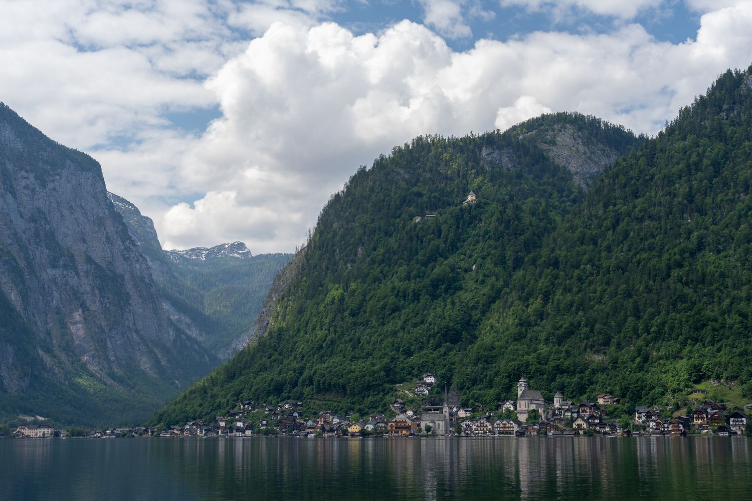 A panoramic view of Hallstatt village nestled between mountains and Lake Hallstatt in Austria under cloudy skies.