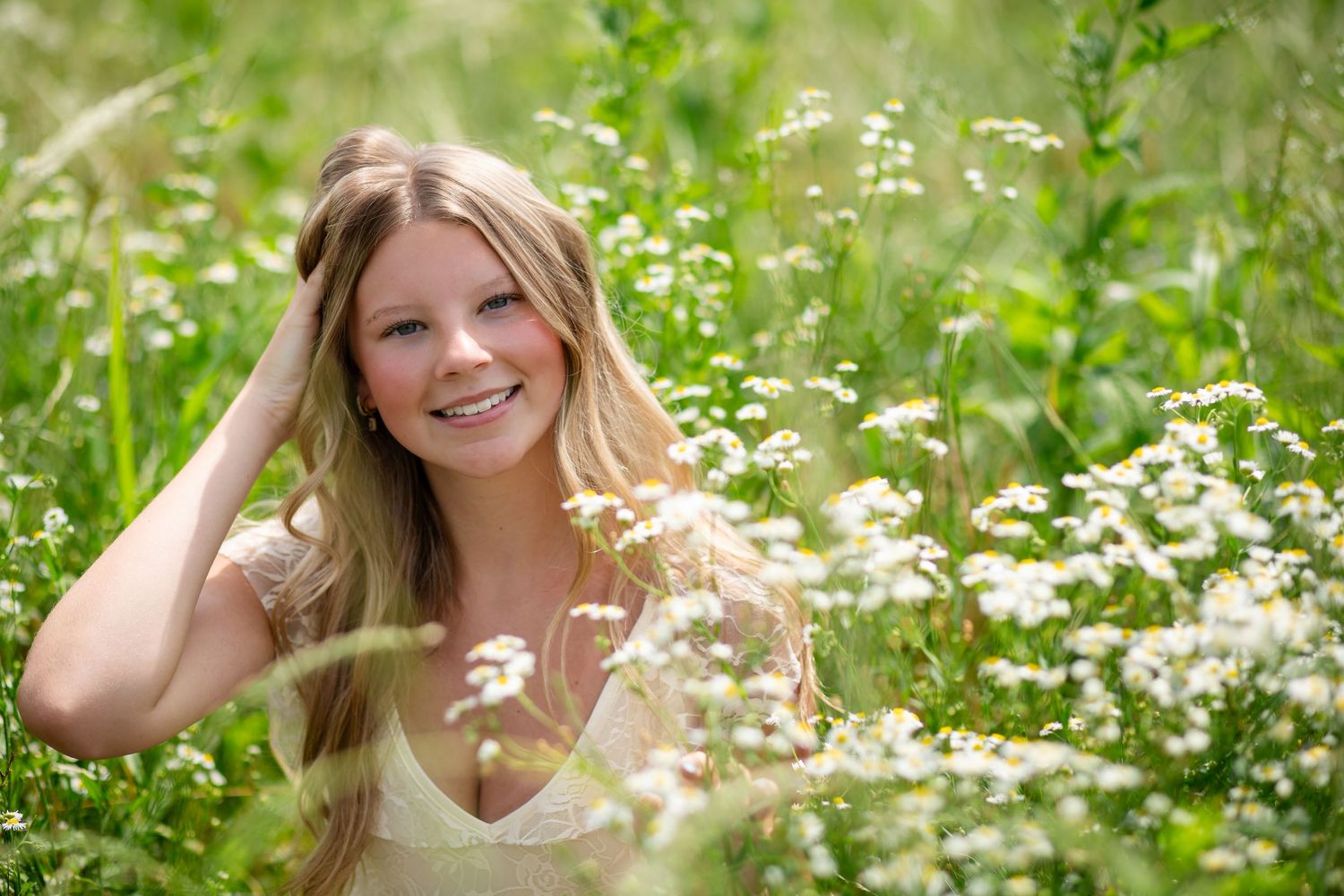 Young blonde woman smiling in a field of white wildflowers on a sunny day.