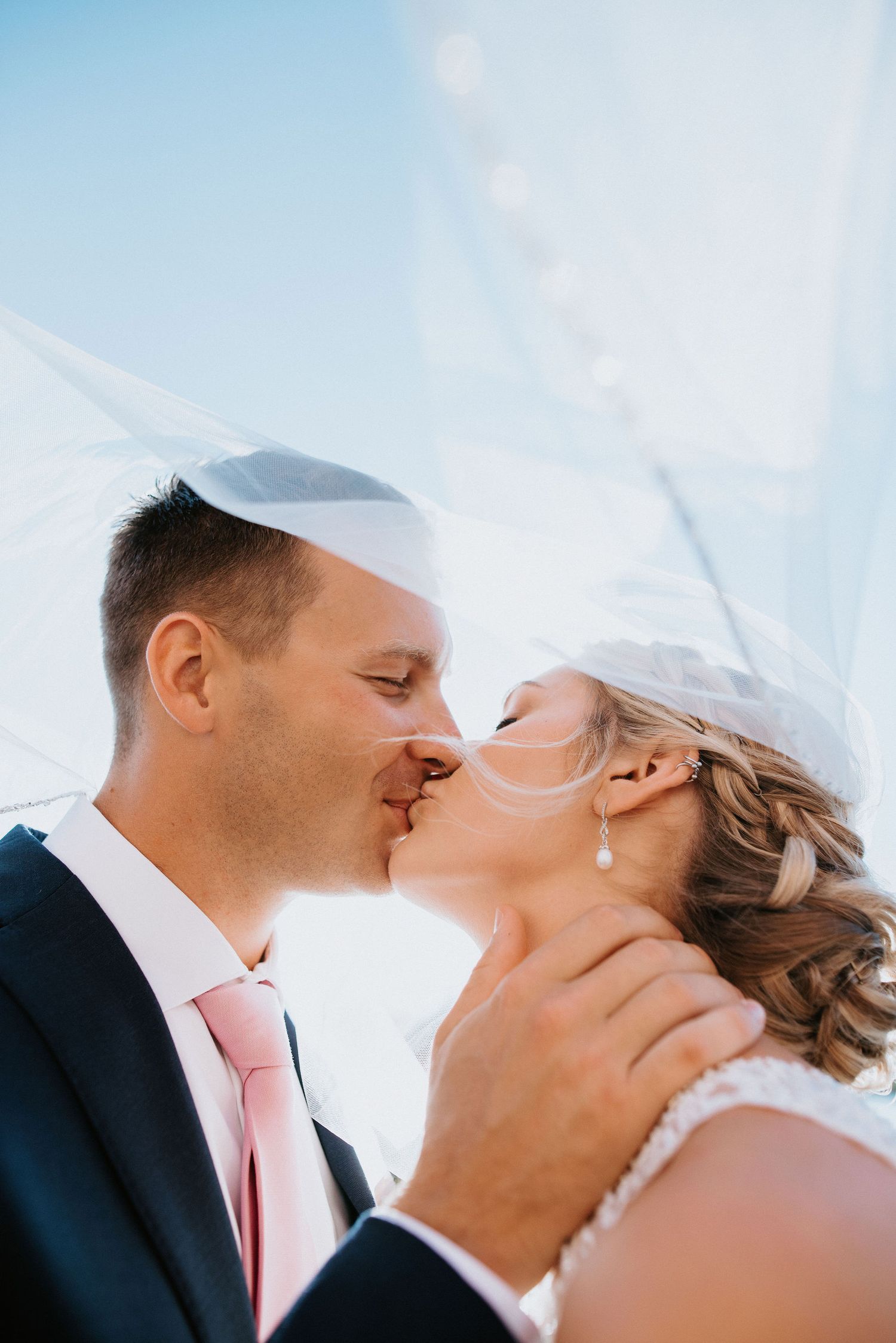 A romantic wedding photo series showing tender kisses between a couple against a bright blue sky.