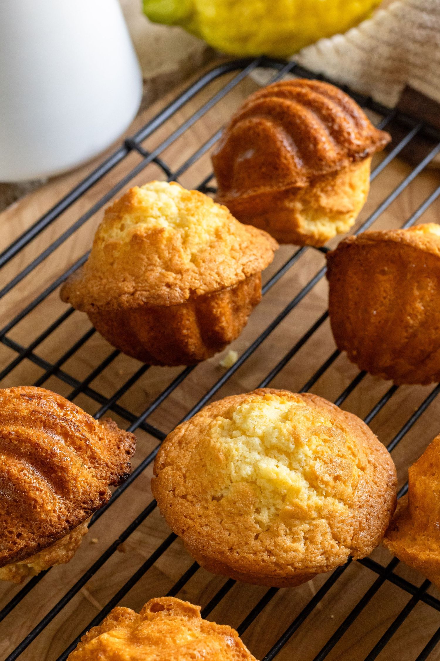 Freshly baked golden muffins cooling on a wire rack, with a ridged bundt-style cake in the foreground.
