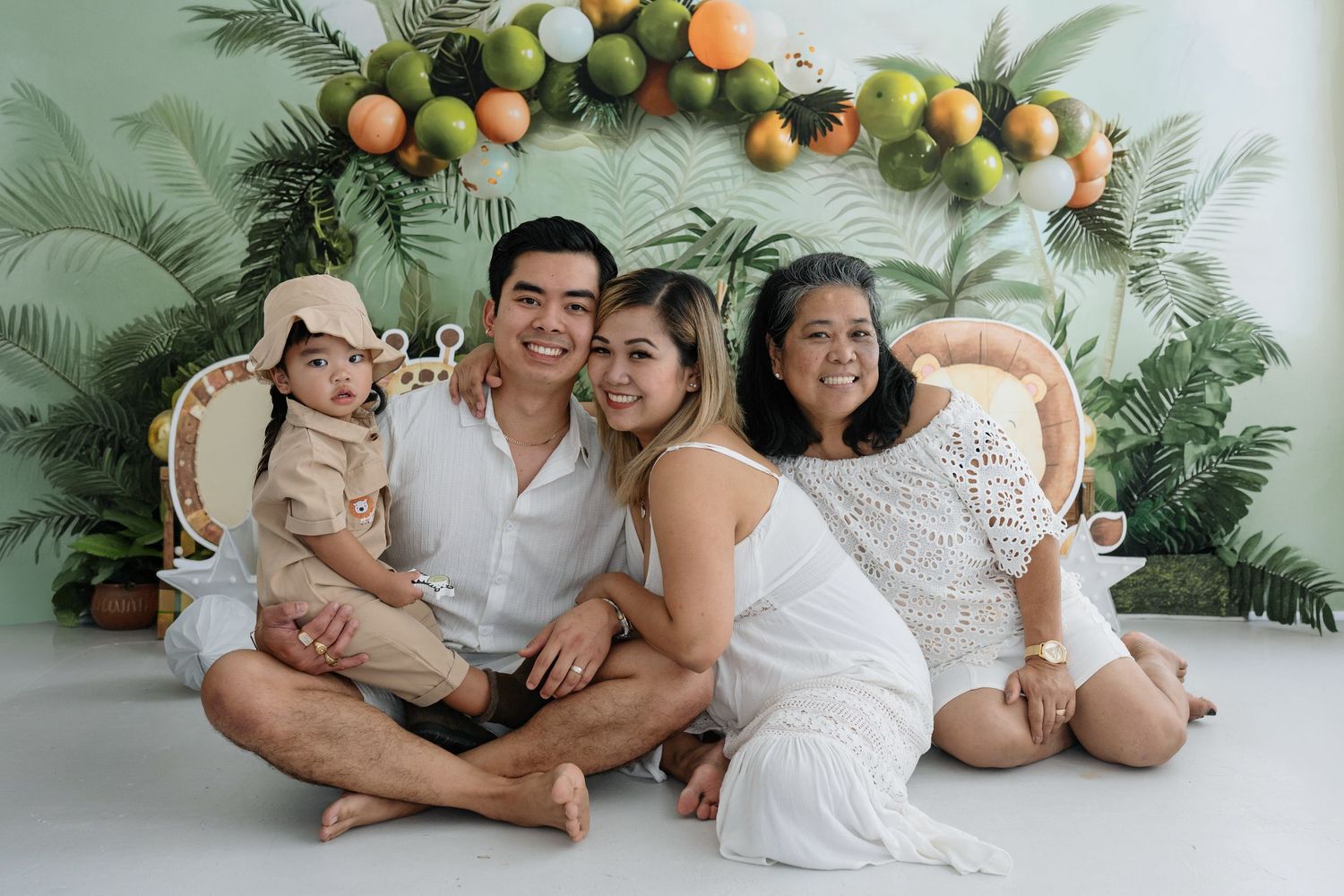 A group in white outfits poses together against a tropical palm leaf backdrop during a photo session.