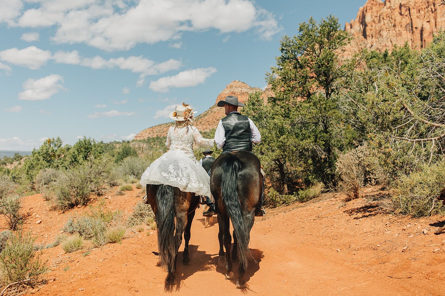 Bride and groom riding horses through red rock Sedona Arizona desert landscape on their wedding day.