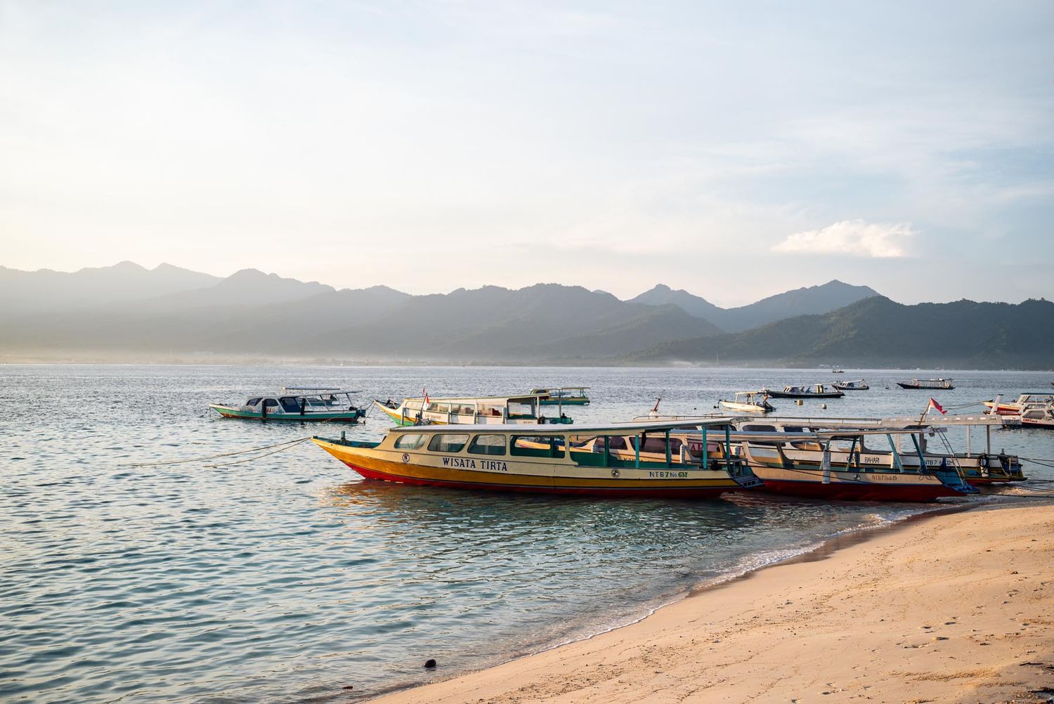A speedboat cruises turquoise waters near a tropical island village with lush green hills and a wooden pier.
