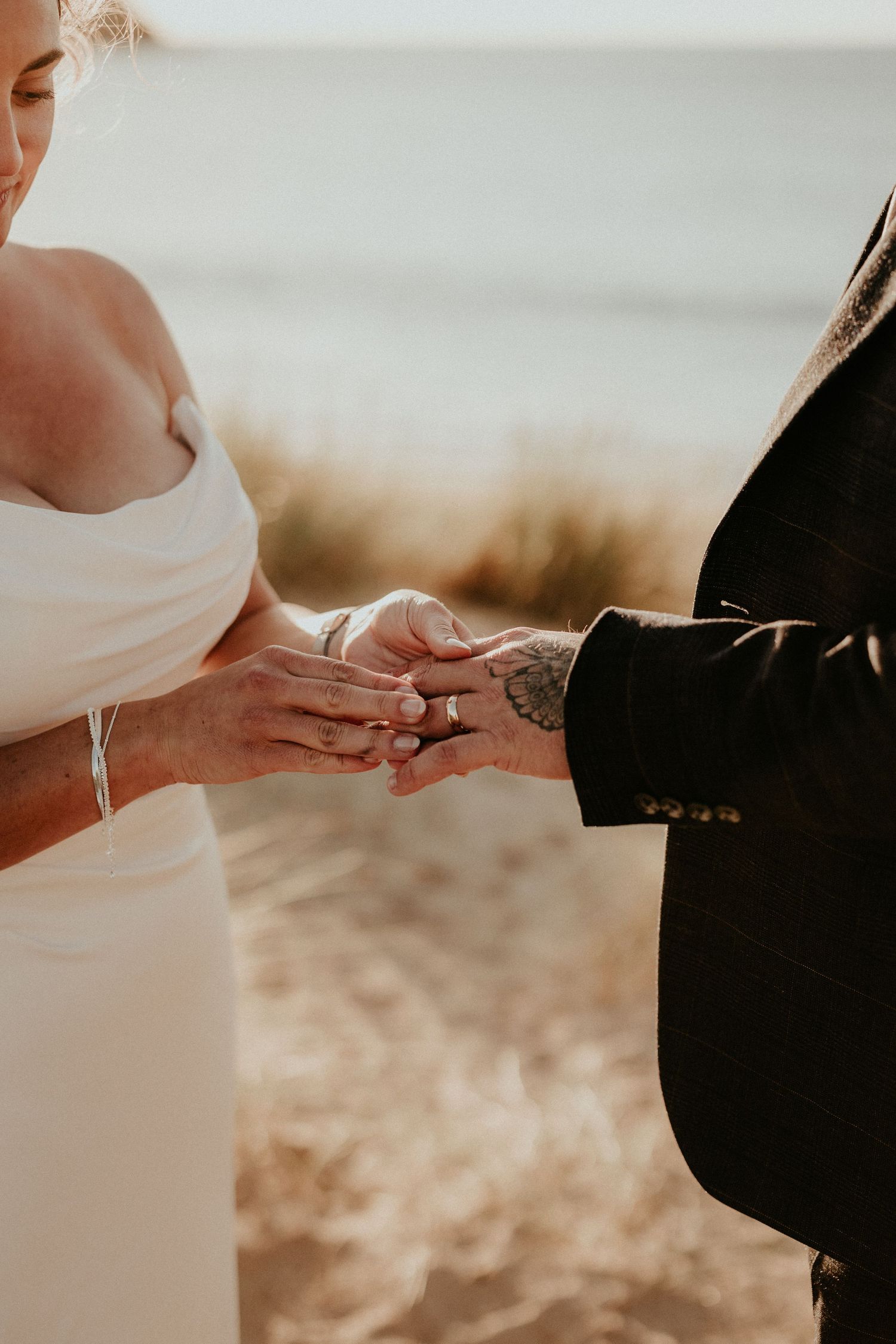 A close-up shot of hands exchanging wedding rings during an outdoor ceremony, with sunlight creating a warm glow. Cornwall wedding photo