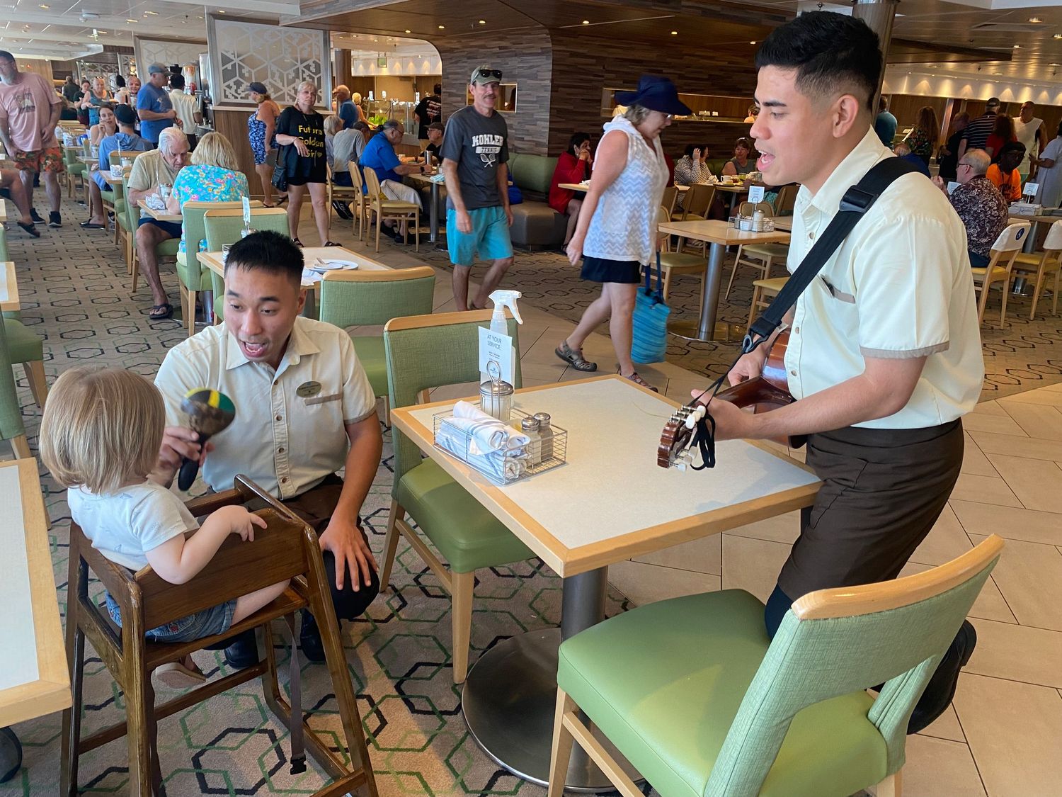 Cruise ship staff entertaining a toddler at a dining table in a busy restaurant onboard a cruise ship.