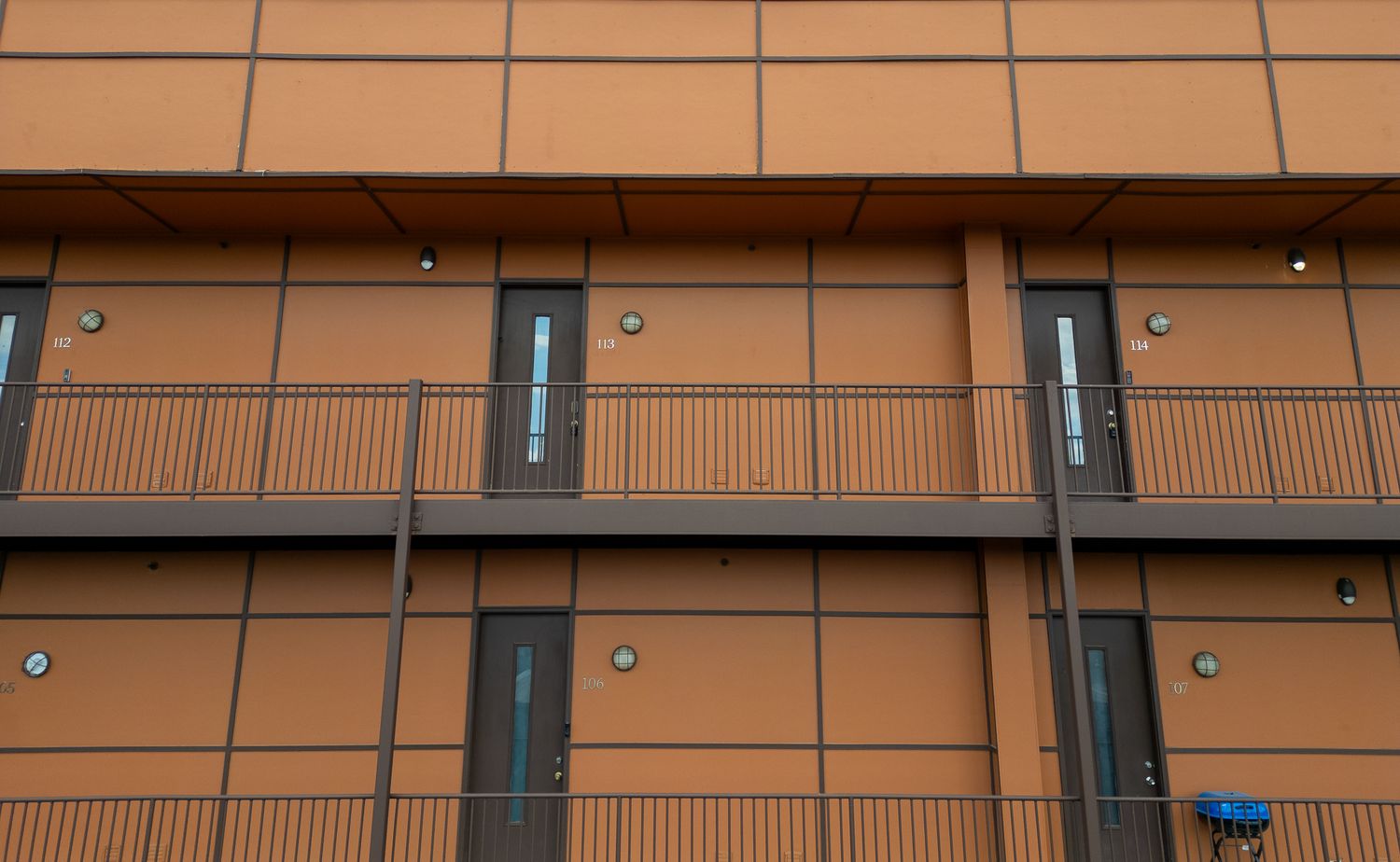 Modern apartment building exterior with brown siding and numbered unit signs mounted on the wall.