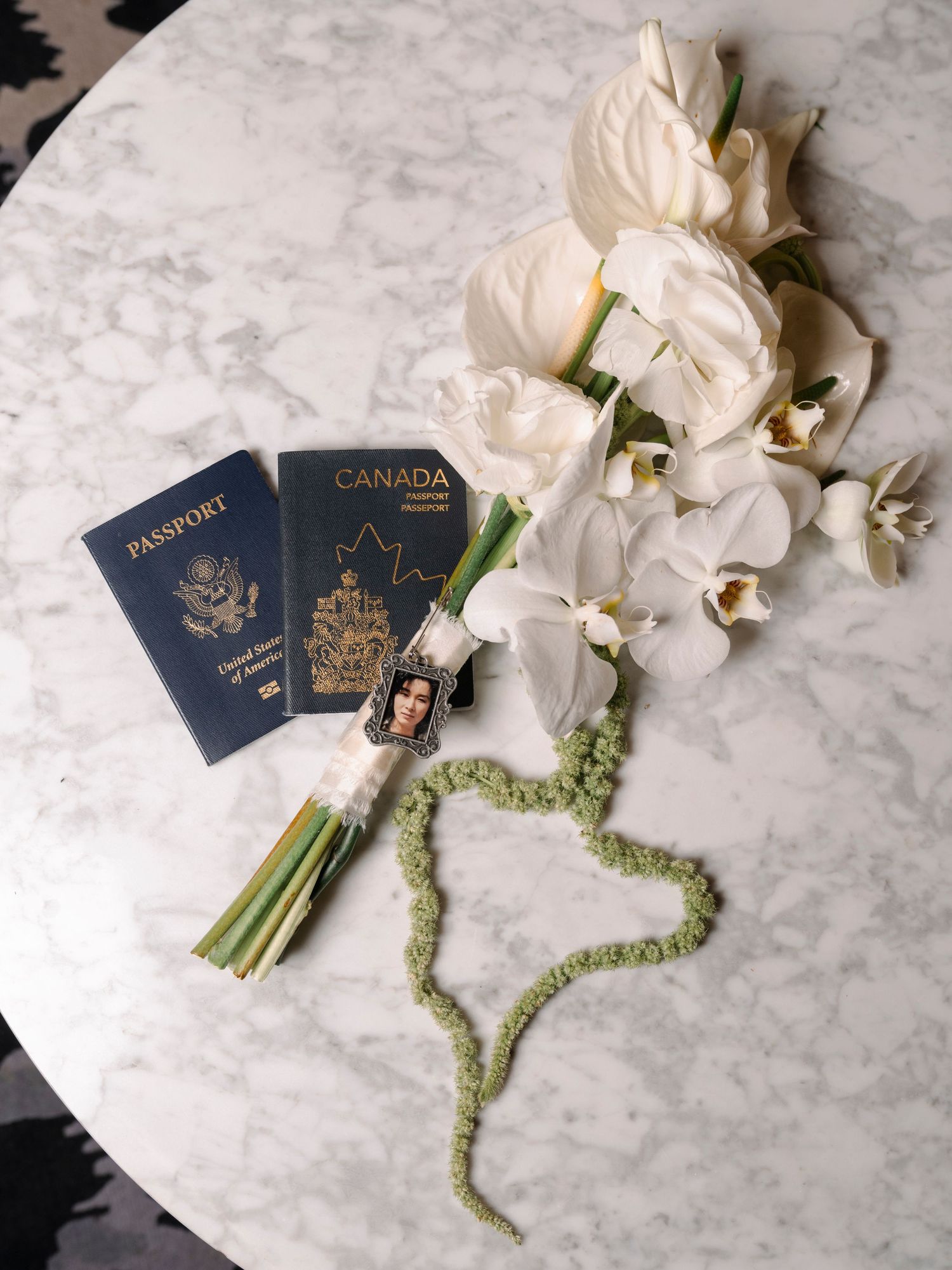 White orchids and navy blue passports arranged on marble surface with green floral ribbon accents.