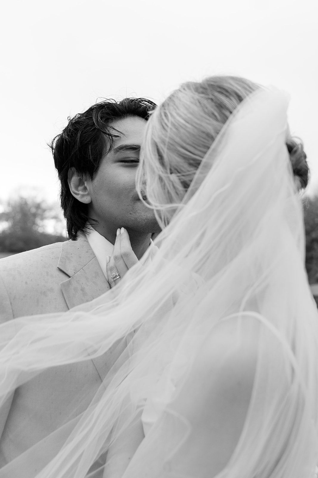 Wedding couple walks through lush green garden path with historic building in background.