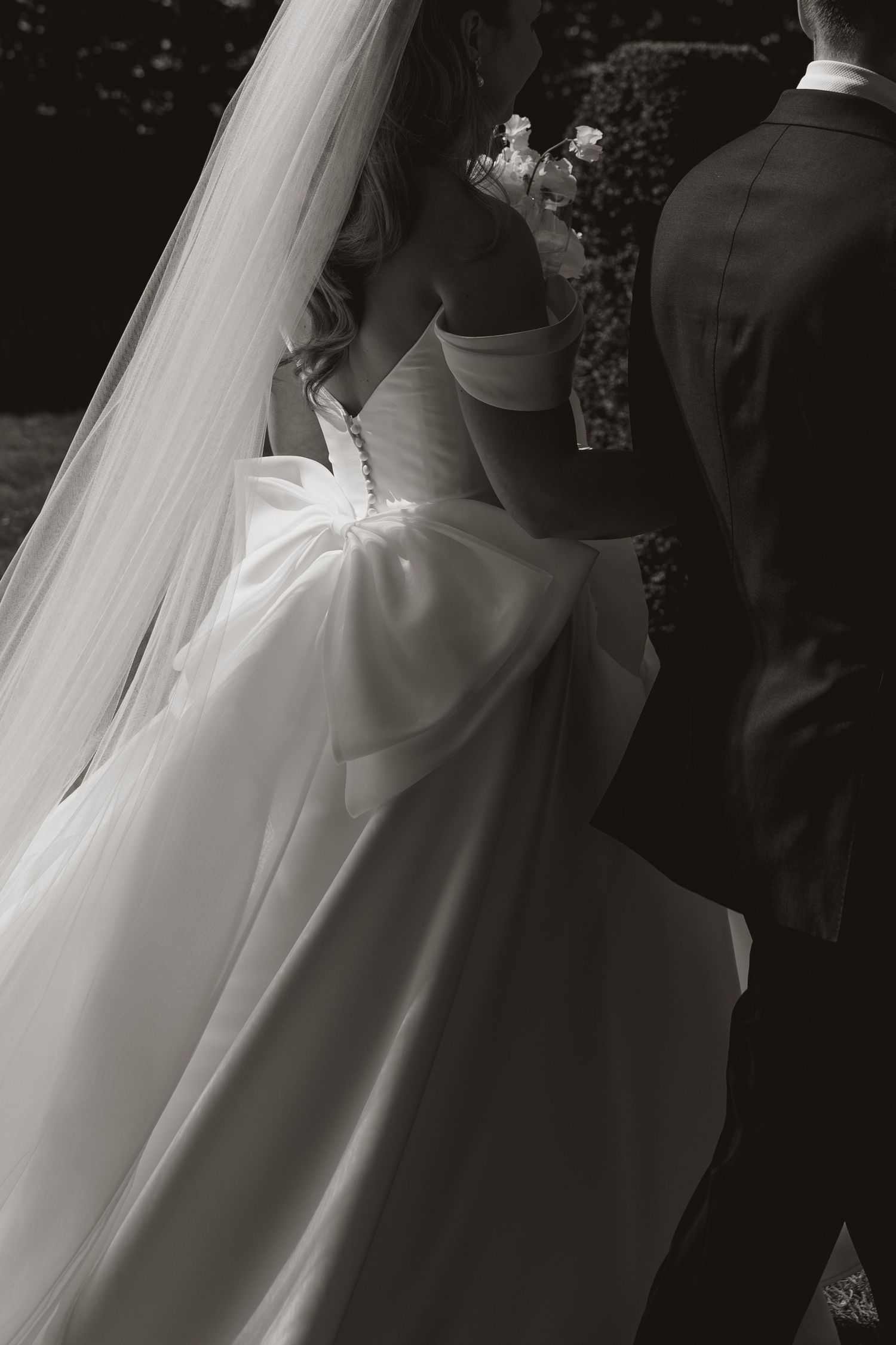 Bride and groom share a kiss on stone steps surrounded by white floral arrangements and lush greenery at outdoor wedding.