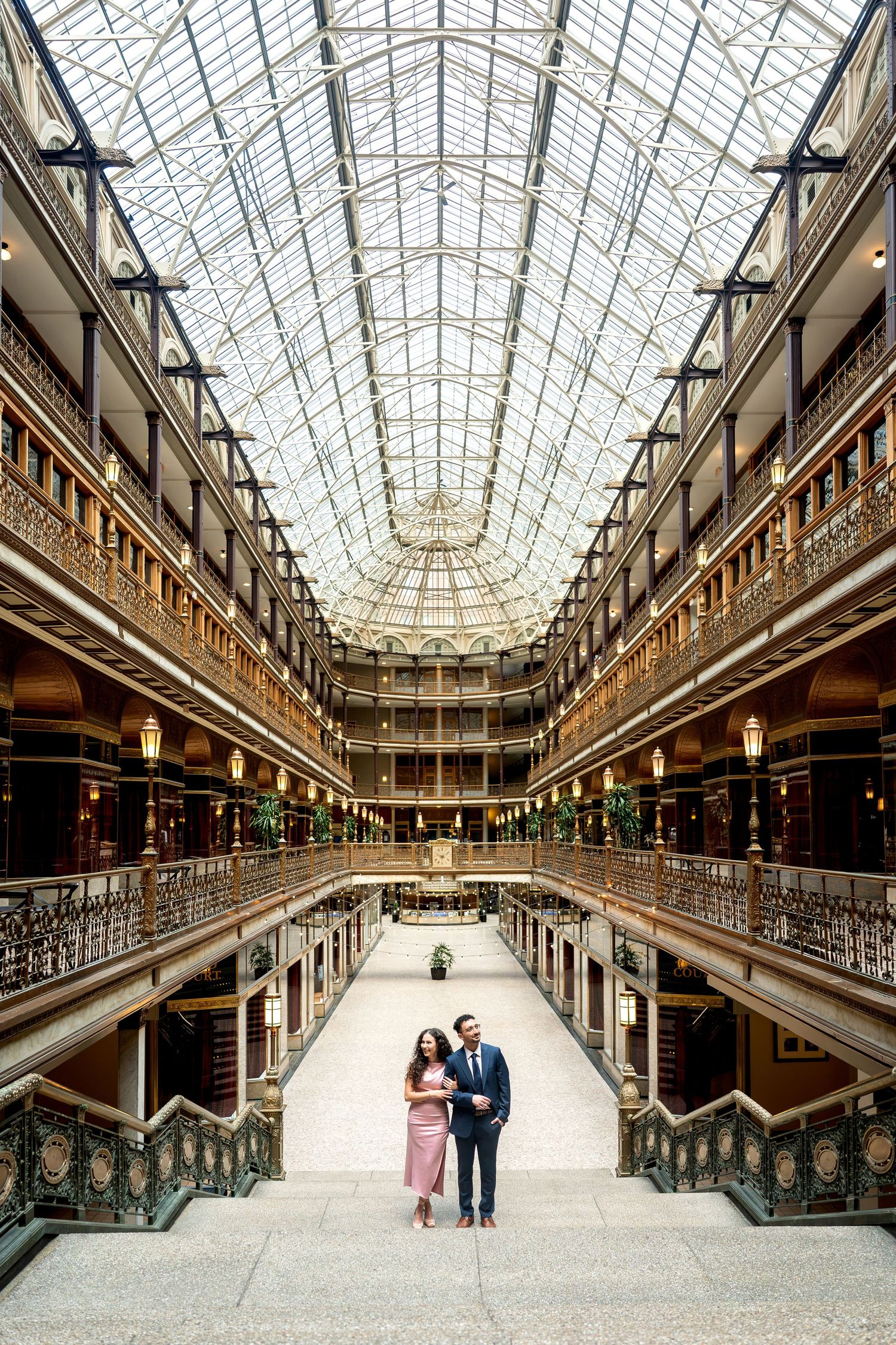 Couple poses in the grand atrium of Cleveland's historic arcade, featuring ornate balconies and a stunning glass ceiling.