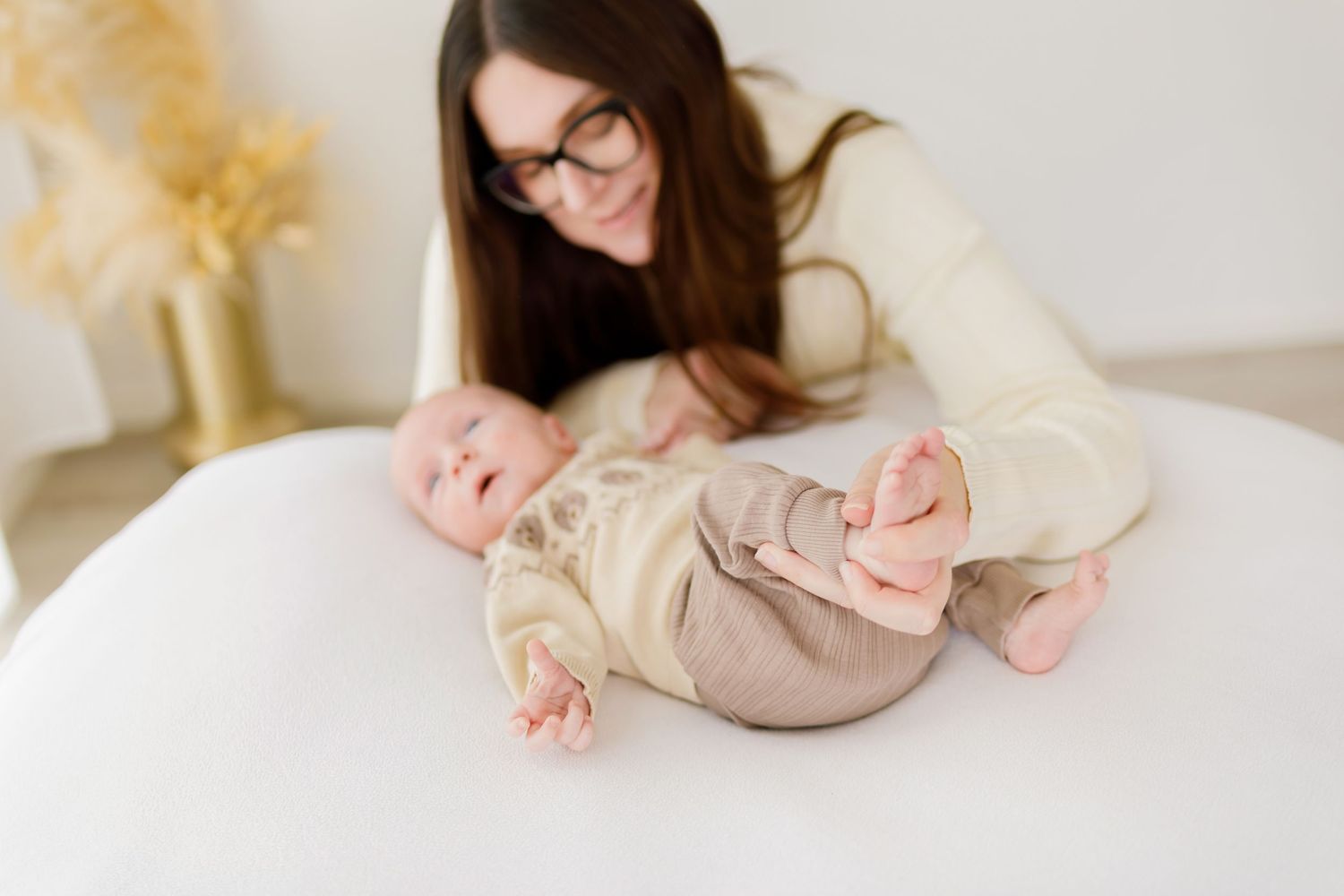 New parents with glasses lovingly holding their newborn baby in a bright, airy white room.
