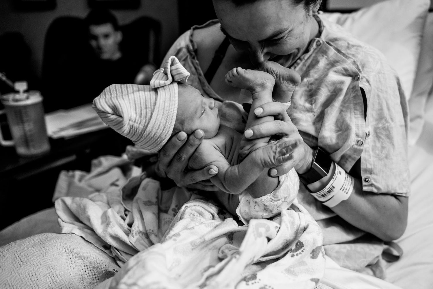 A caregiver tenderly holds and examines a swaddled newborn in black and white.