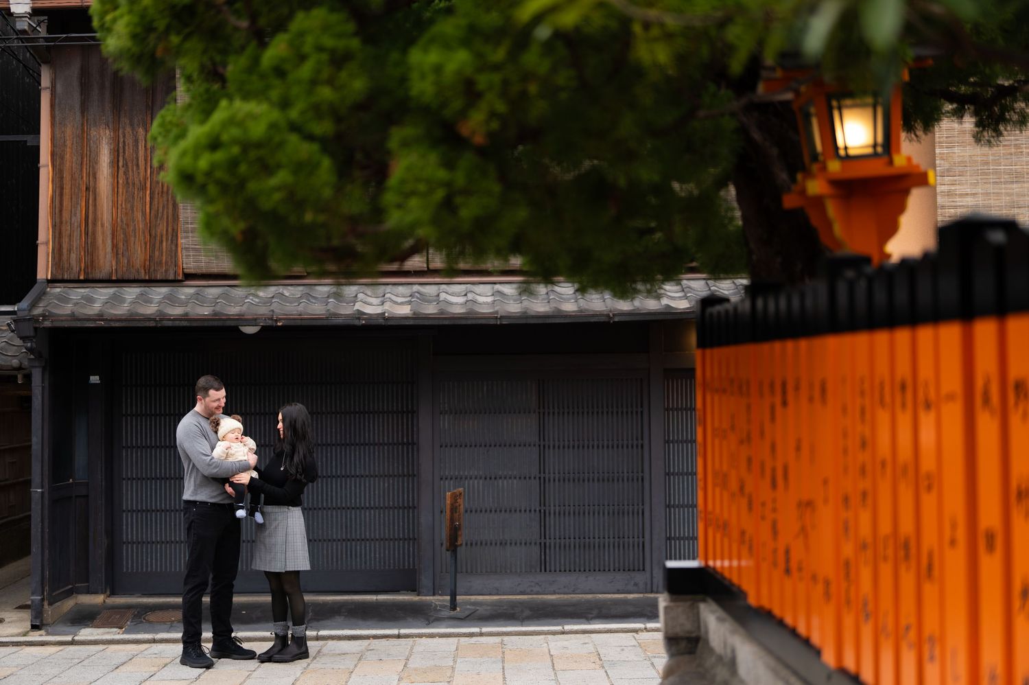 Couple with baby standing near iconic orange torii gates and traditional architecture in Kyoto Japan.