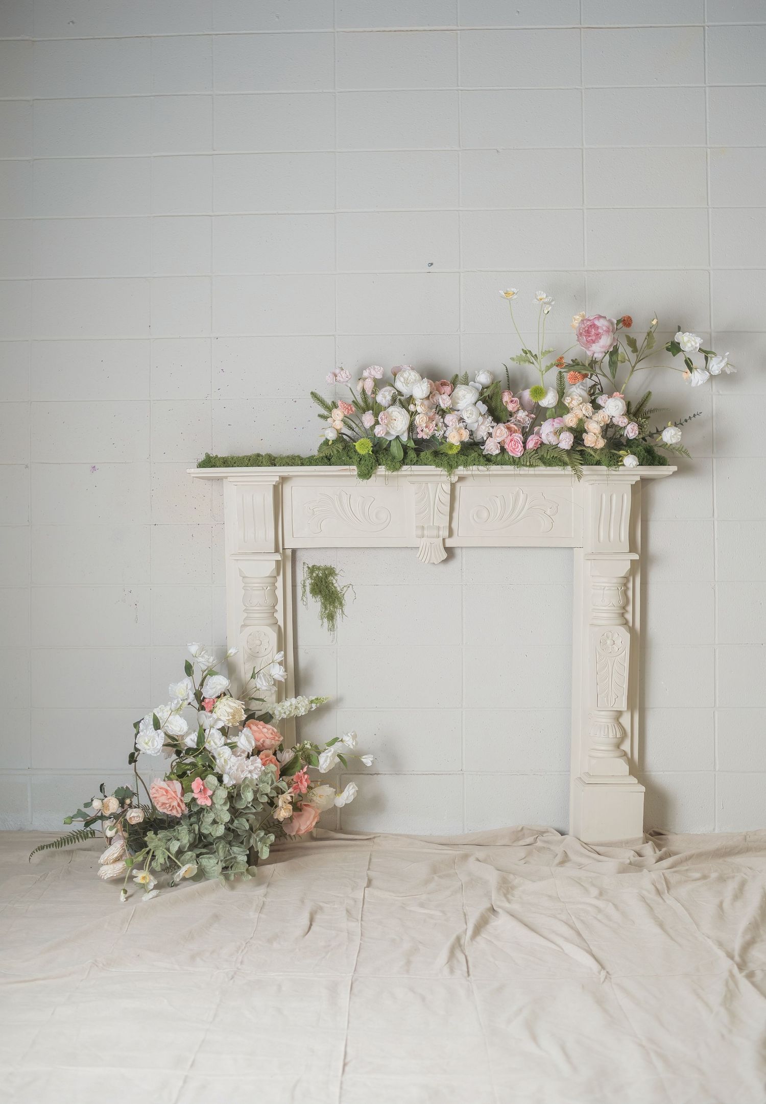 White ornate fireplace mantel decorated with pink and white floral arrangements on top and floor beside it.