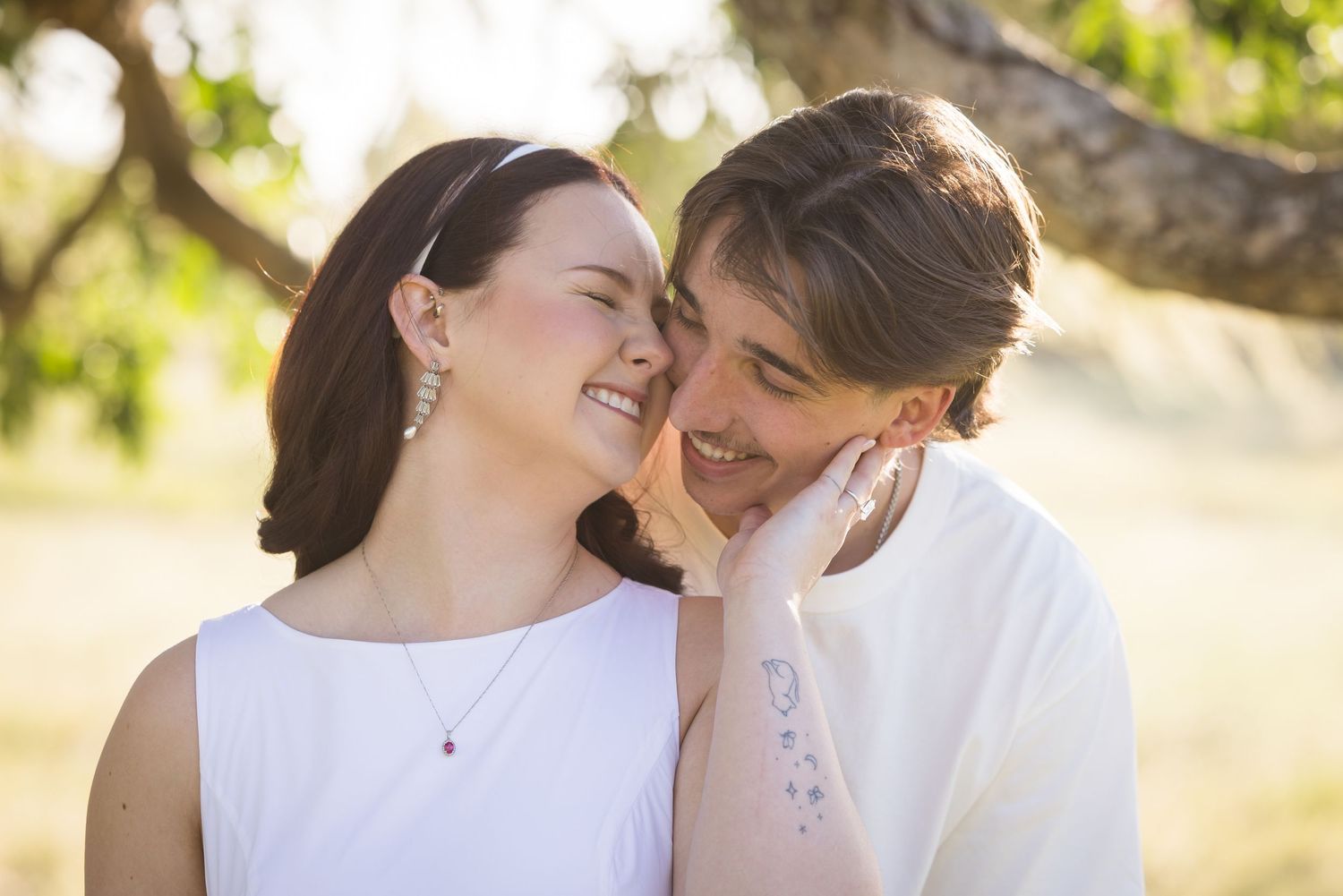 Black and white photo of a smiling couple sharing a tender moment outdoors under a tree.