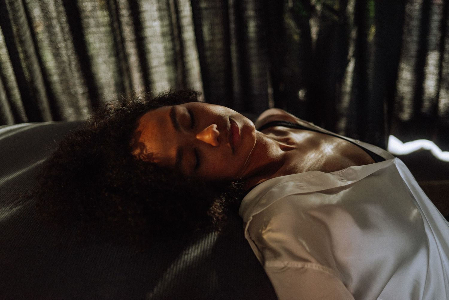 Woman lying down with eyes closed in dramatic lighting with shadows from window blinds falling across their face.