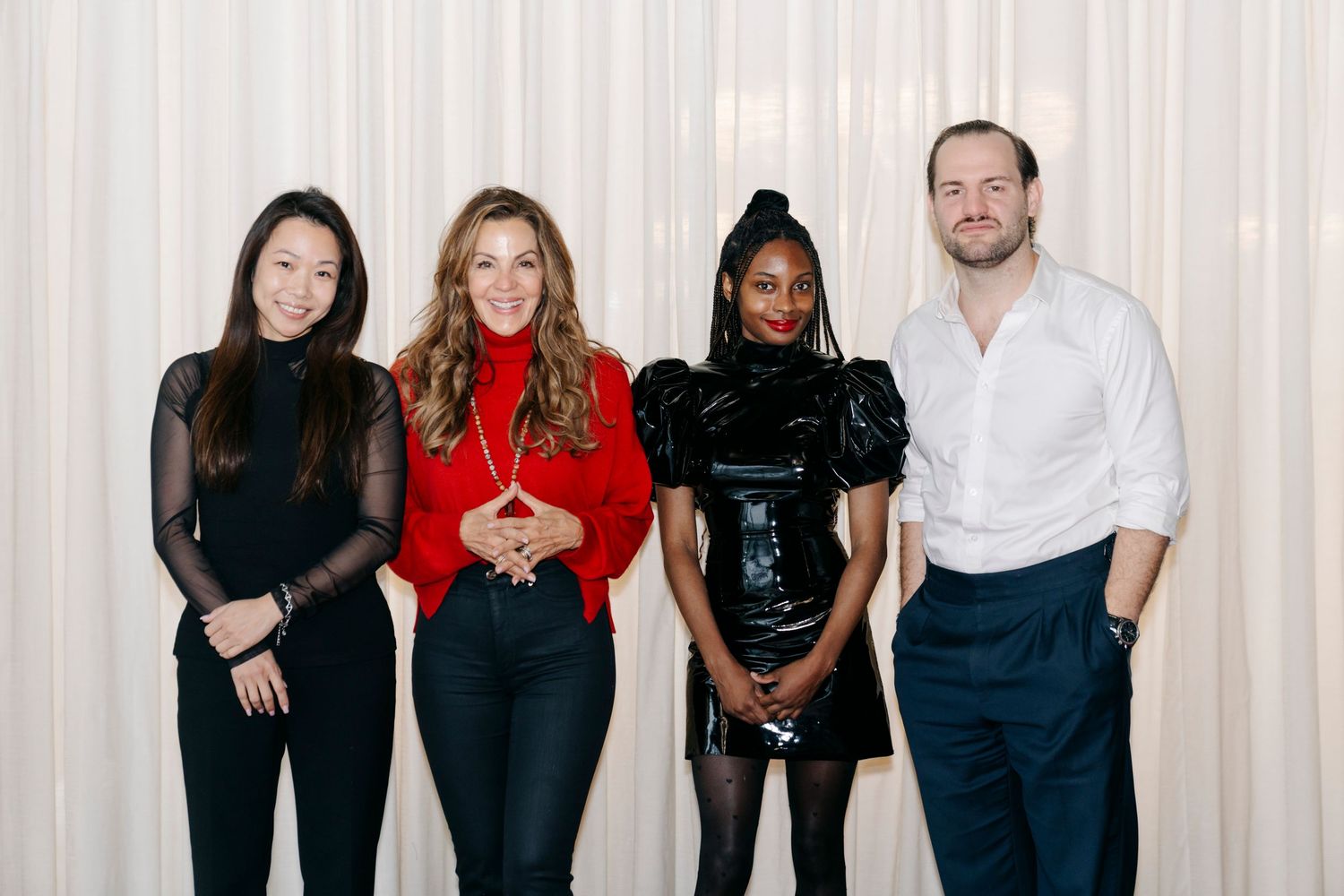 A group of people wearing casual black and red outfits pose together against a white curtain backdrop.