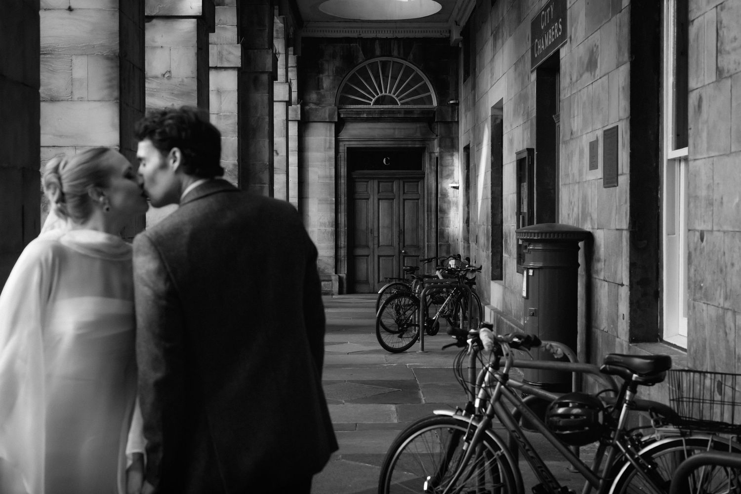 Wedding party celebrates with laughter outside historic City Chambers building in formal attire.