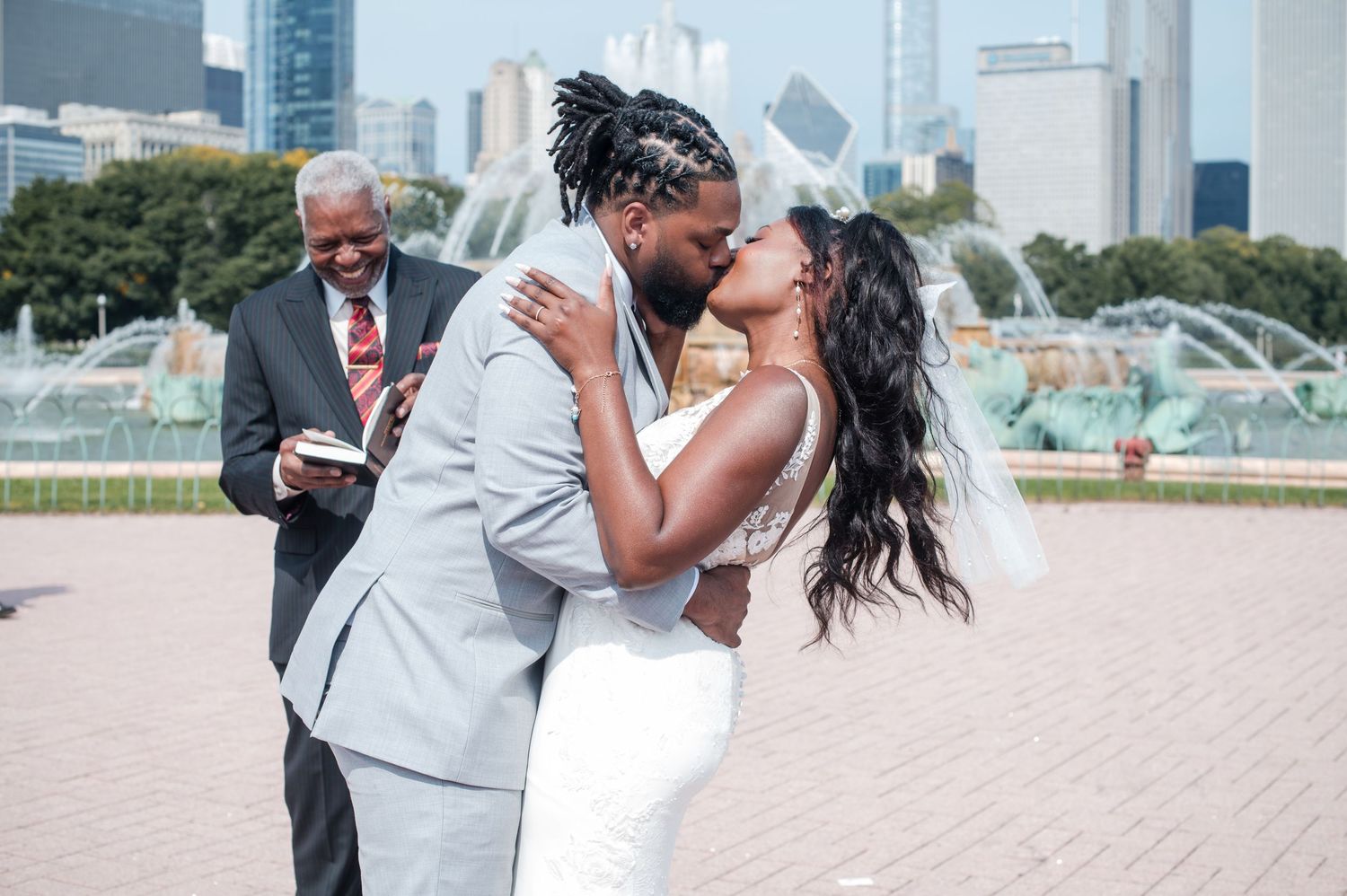 Newlywed couple sharing first kiss at outdoor wedding ceremony near Buckingham Fountain in Chicago.