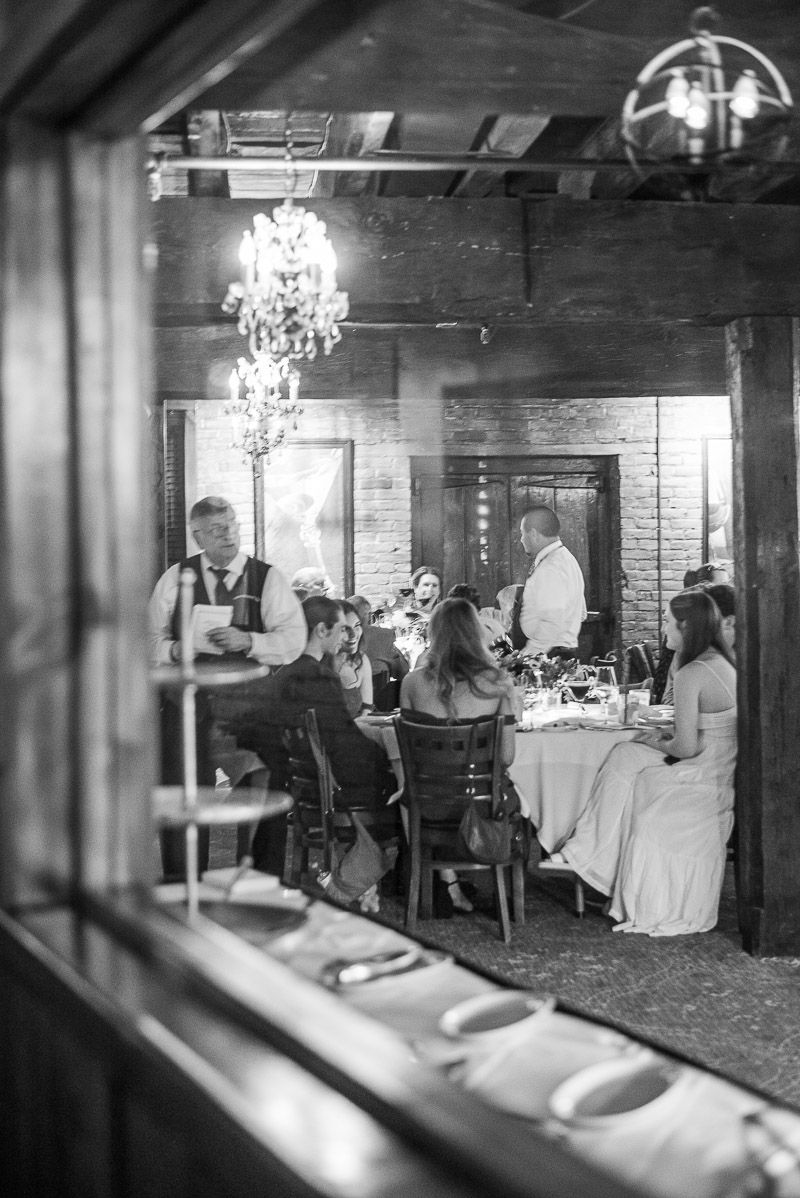 Rustic dining room interior with exposed brick walls, hanging plants, and elegant table settings in natural light.