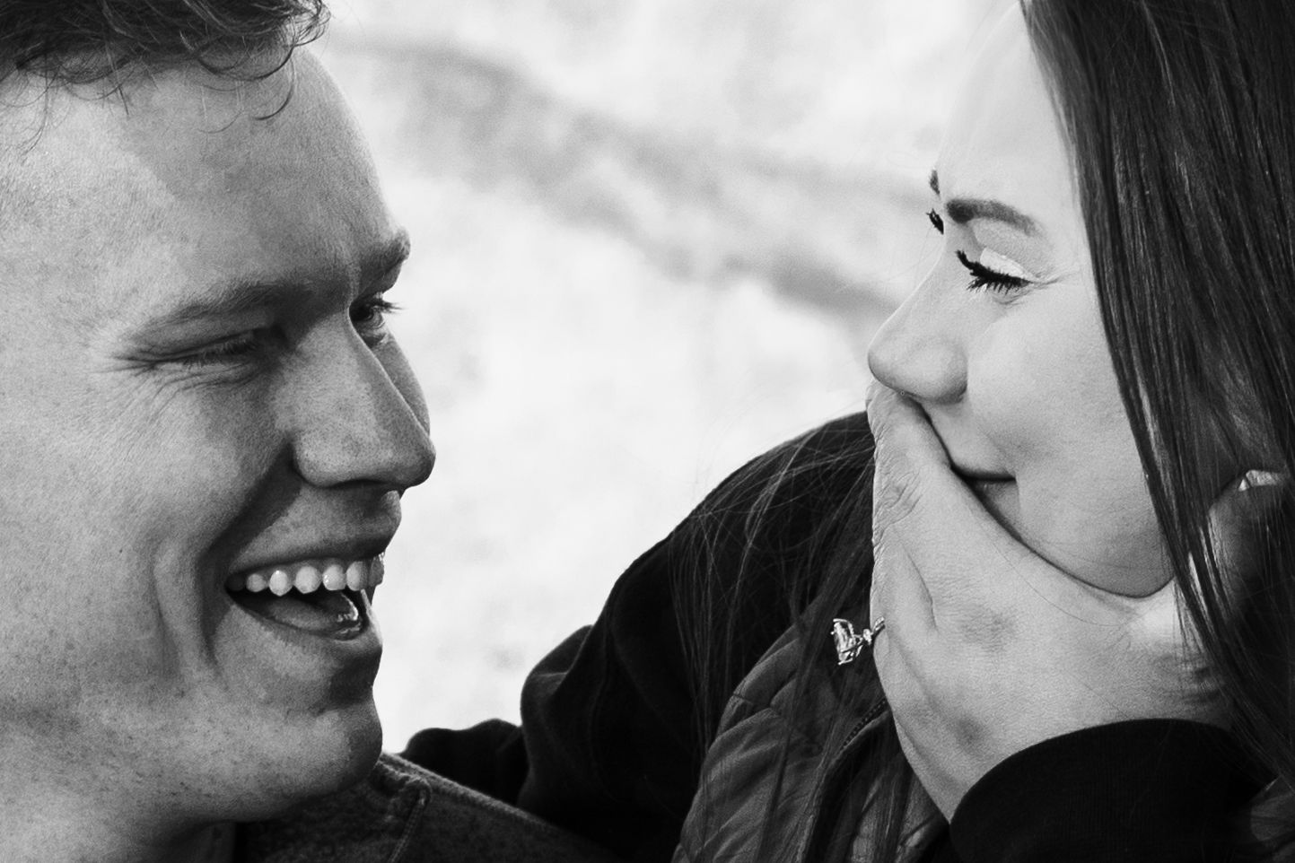 Black and white photo of a couple embracing under a grand stone archway, sharing a romantic moment.
