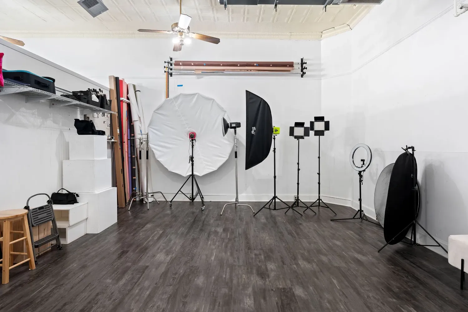 Professional photography studio with lighting equipment, umbrellas, and ring lights on dark hardwood floors.