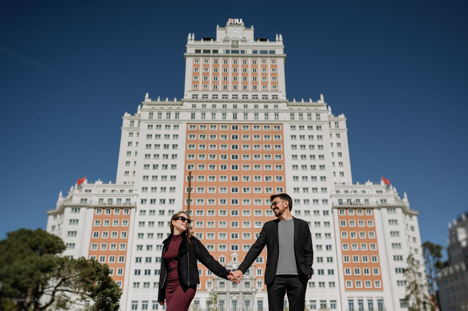 Couple holding hands in front of the iconic Edificio España skyscraper in Madrid, Spain.