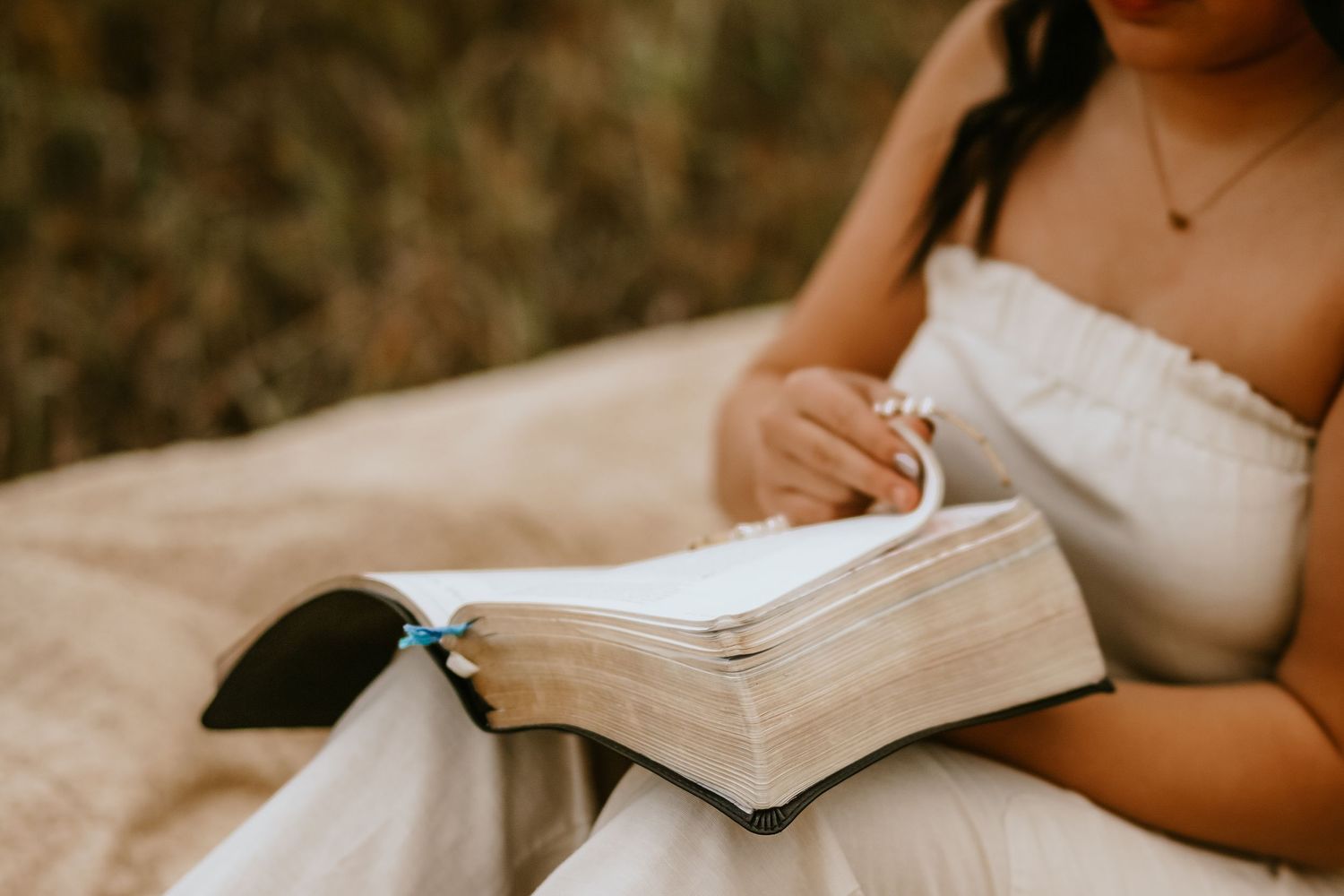 Woman in white dress reading a Bible outdoors in a natural setting.