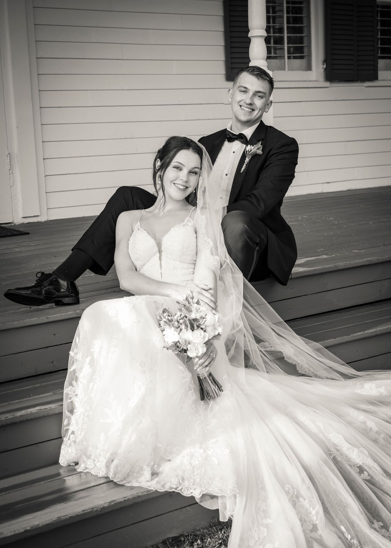 Black and white photo of a bride and groom walking hand in hand on a road, smiling on their wedding day.