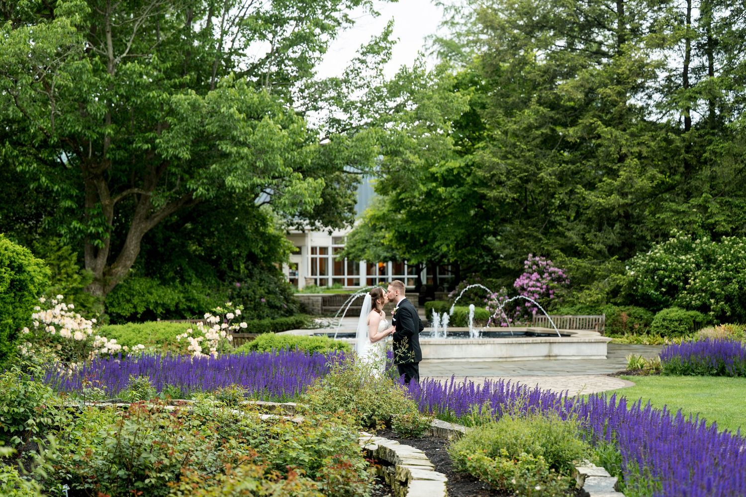 Bride and groom share a romantic kiss surrounded by lush green forest and ferns at an outdoor woodland wedding.