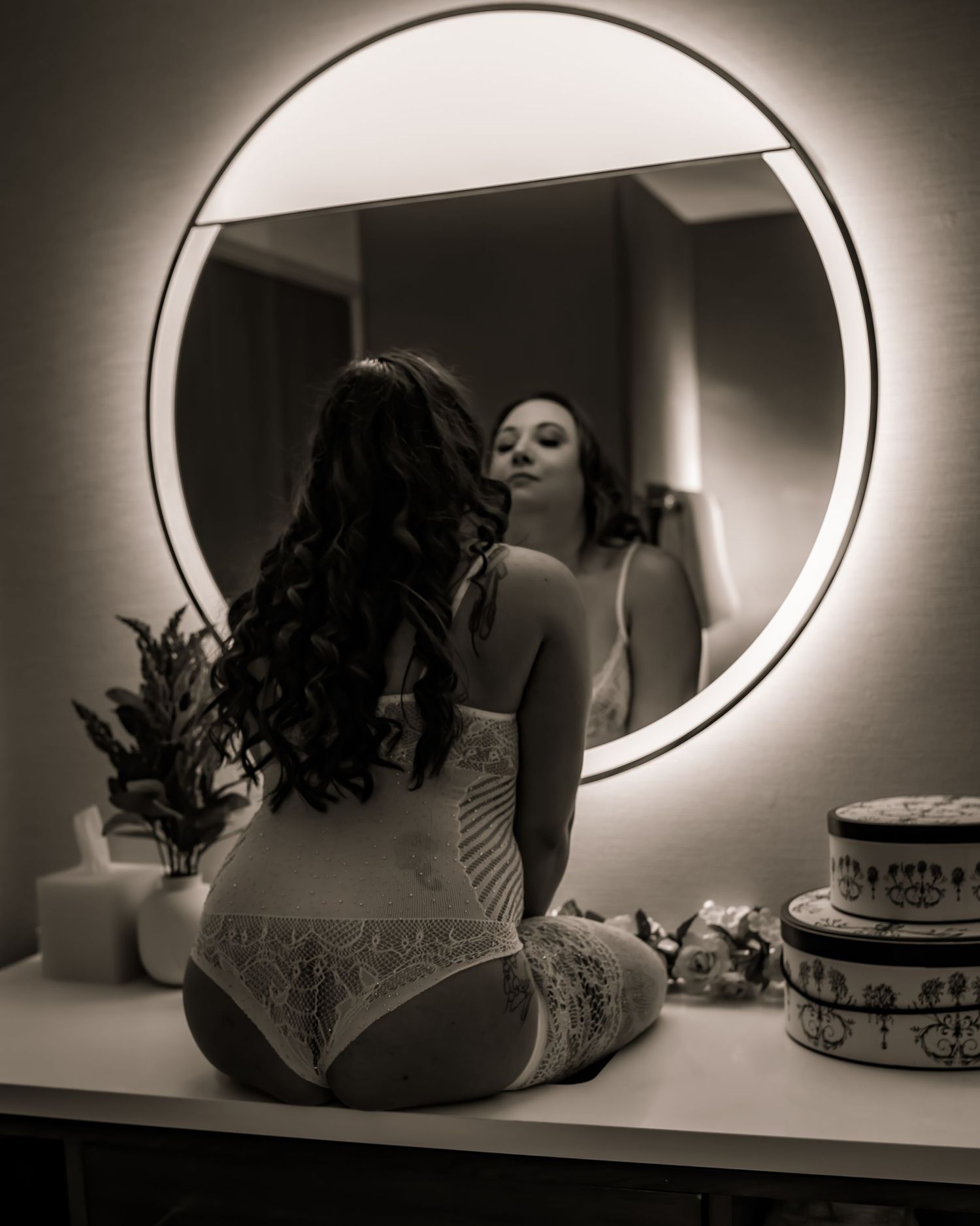 Artistic boudoir photo with illuminated round mirror and moody lighting.