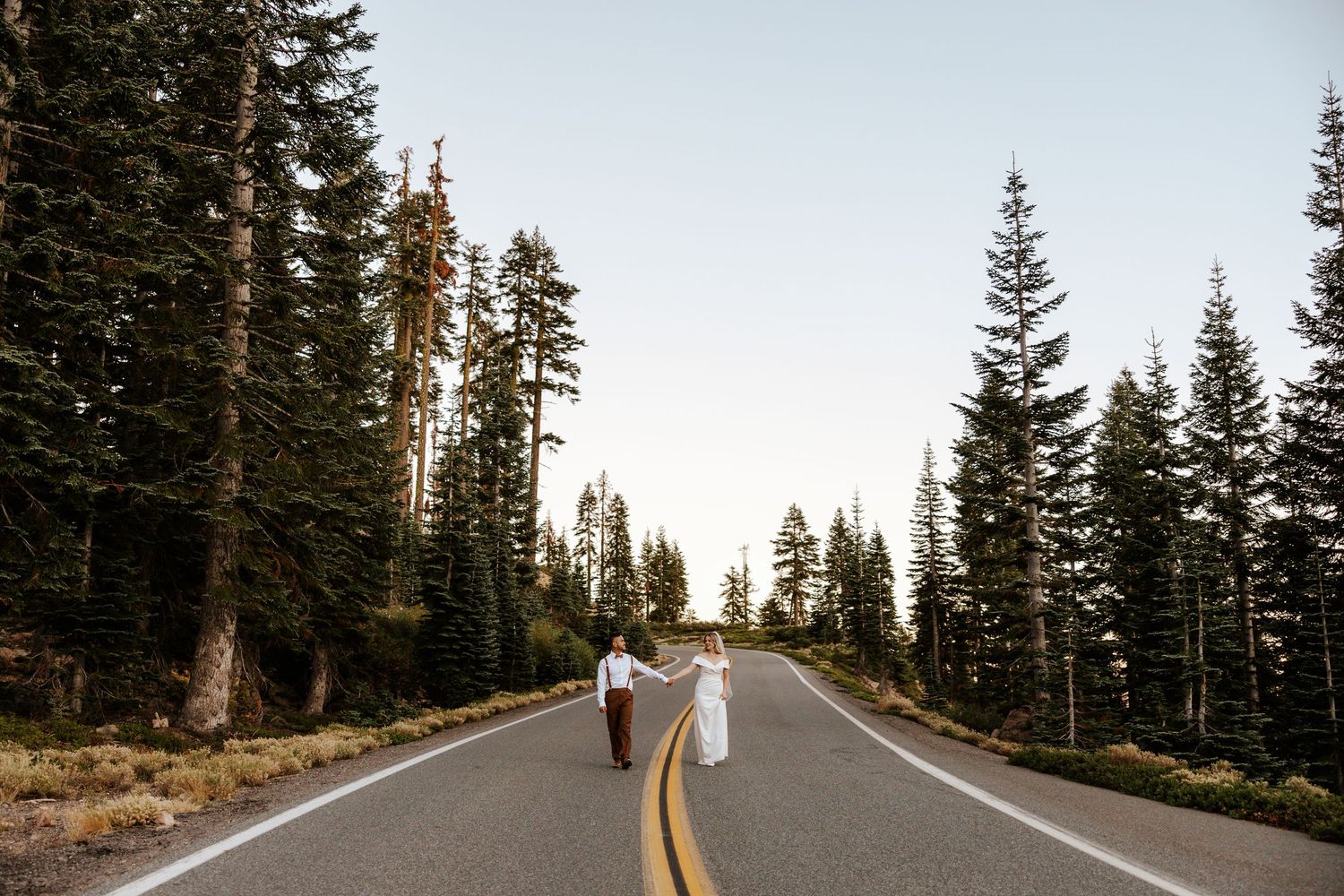 Eloping couple walking in the street with alpine trees lining either side in mount shasta, california elopement