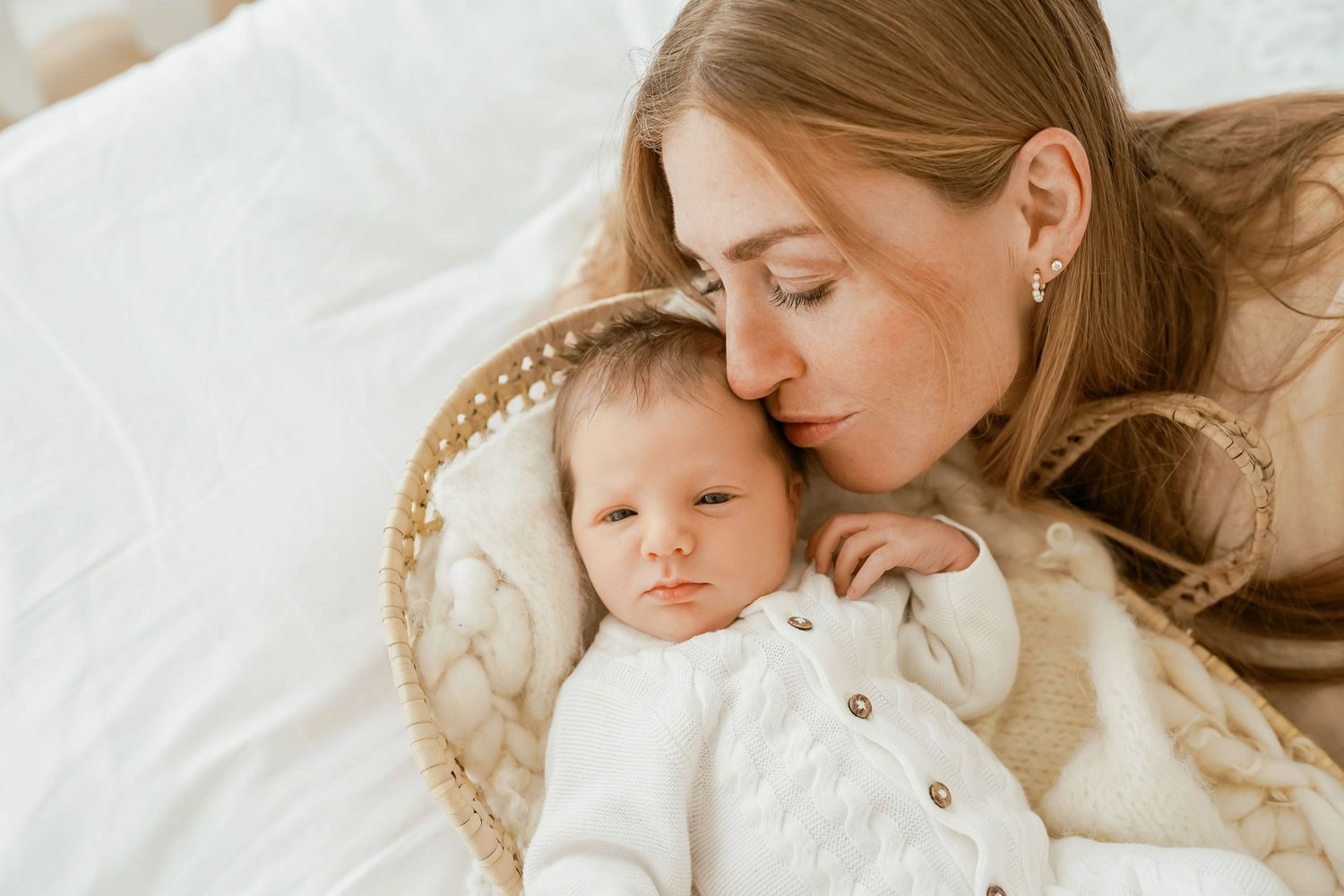 A tender moment captured of parent and baby resting together on white bedding.
