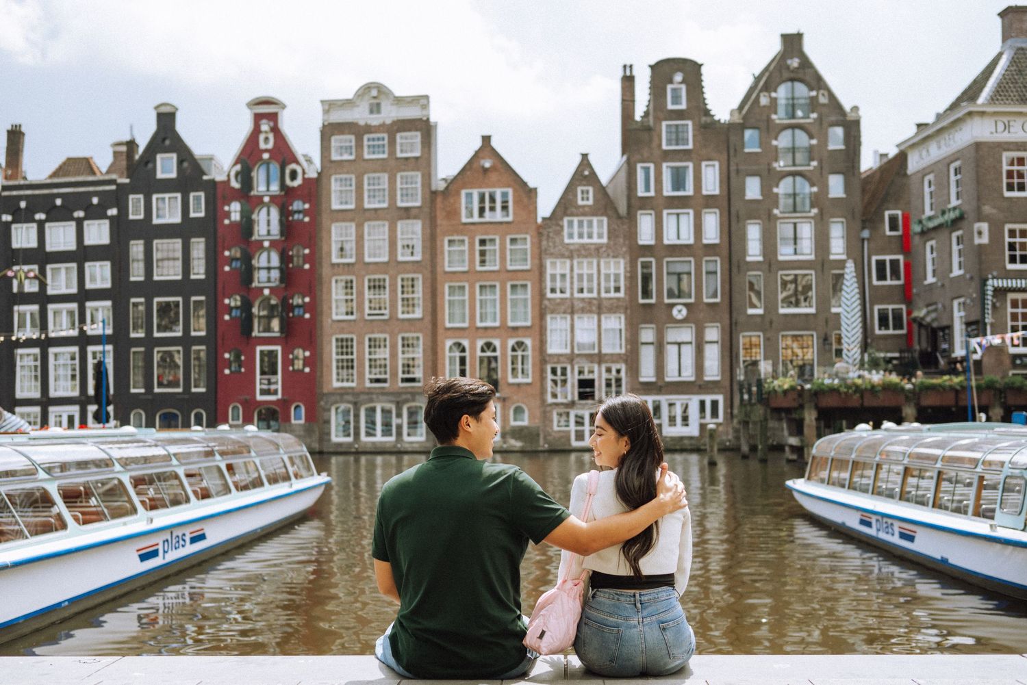 Happy couple with Amsterdam canal houses in the background – a popular location for photoshoots in Amsterdam.