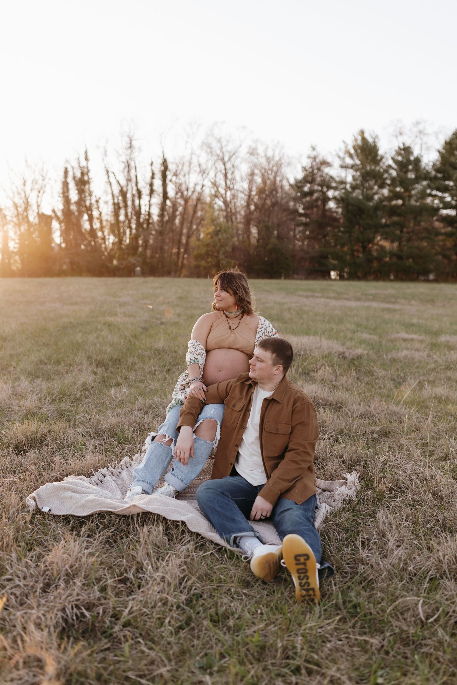 Couple sits on blanket in sunlit field at sunset.