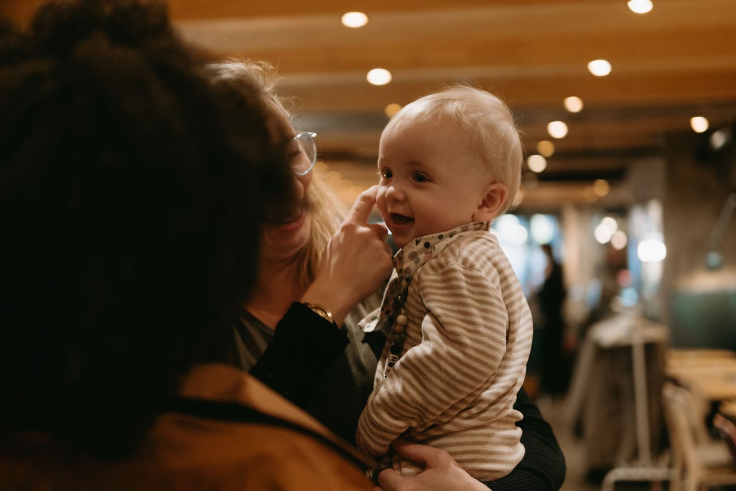 a mother holding her baby that is smiling while she strokes his cheeks while being captured by event photographer in Stockholm