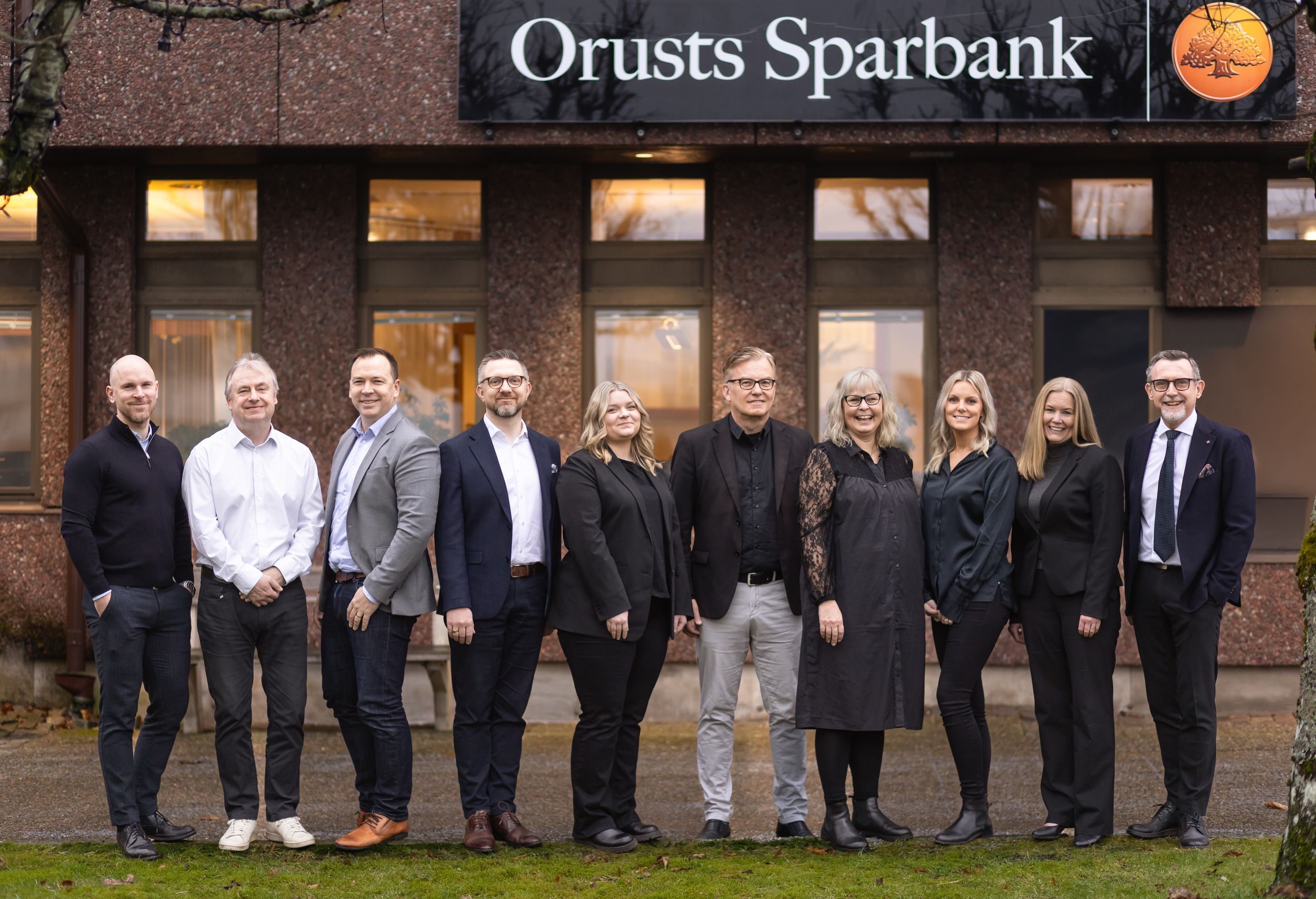 A group of business professionals stands lined up outside the entrance of Orusts Sparbank bank building.