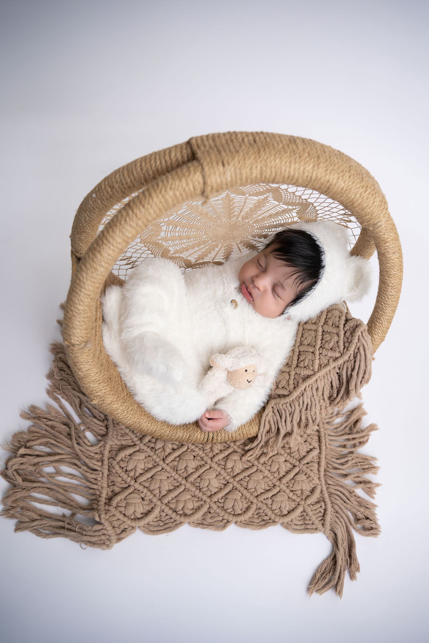 A sleeping newborn nestled in a cozy macrame basket with soft white padding and beige woven decorative elements.