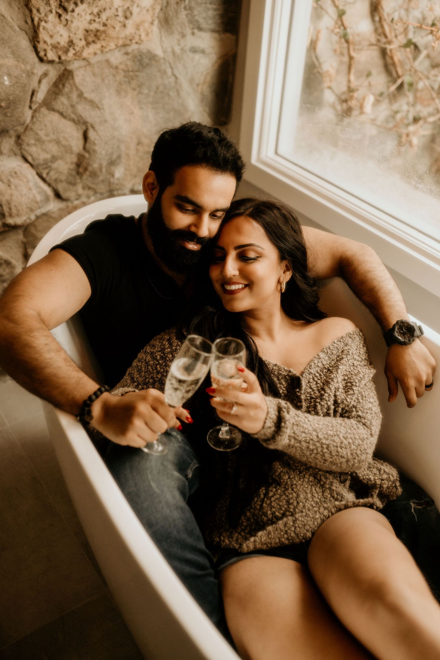 Romantic couple toasting champagne while relaxing together in a vintage bathtub.