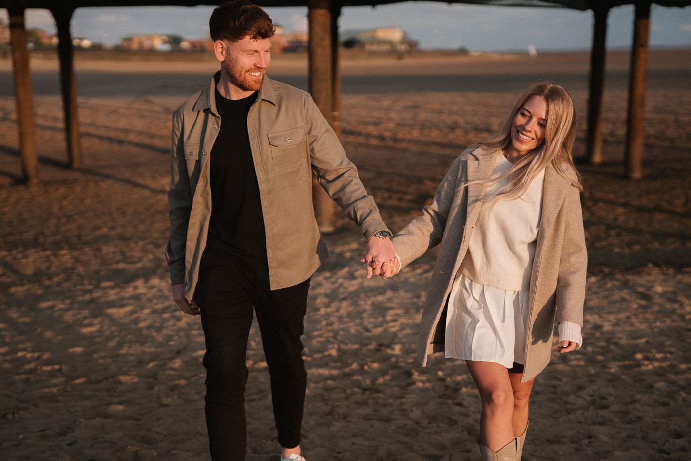 A couple holding hands and walking together during golden hour sunset at a beach.