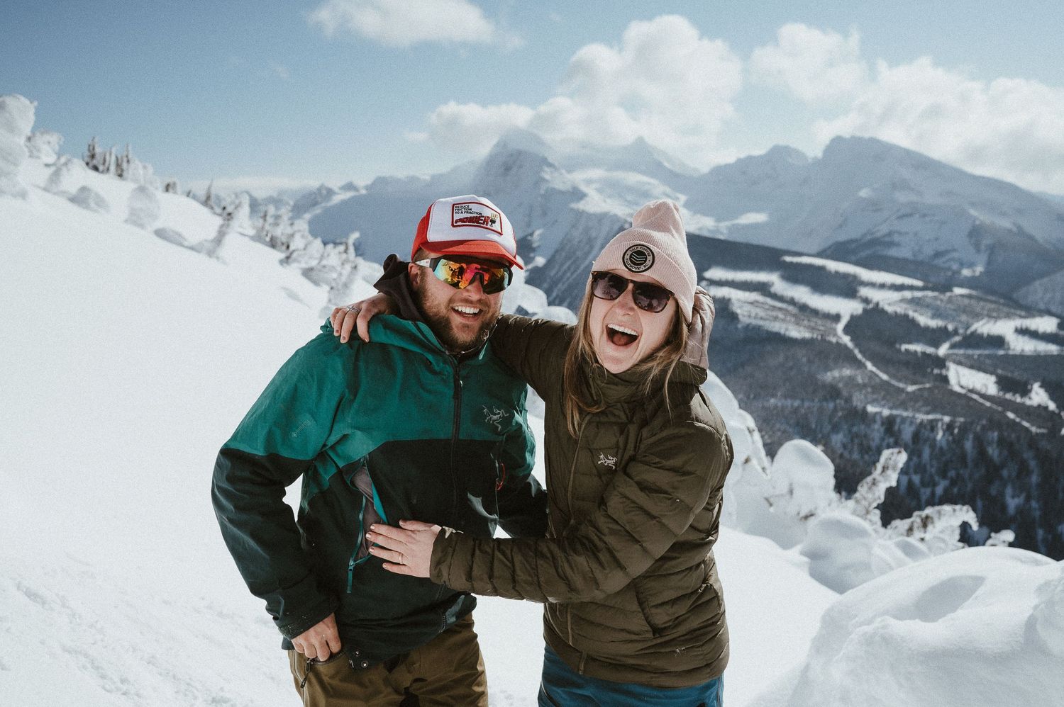 Winter adventure couple laughing together on snowy mountain peak.