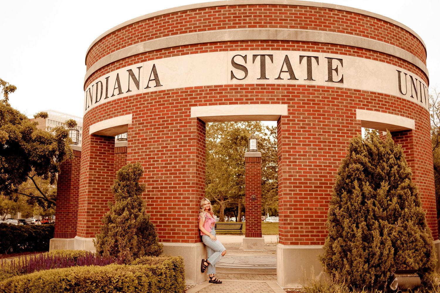 A person in a beige sweater stands near a brick university entrance during autumn.