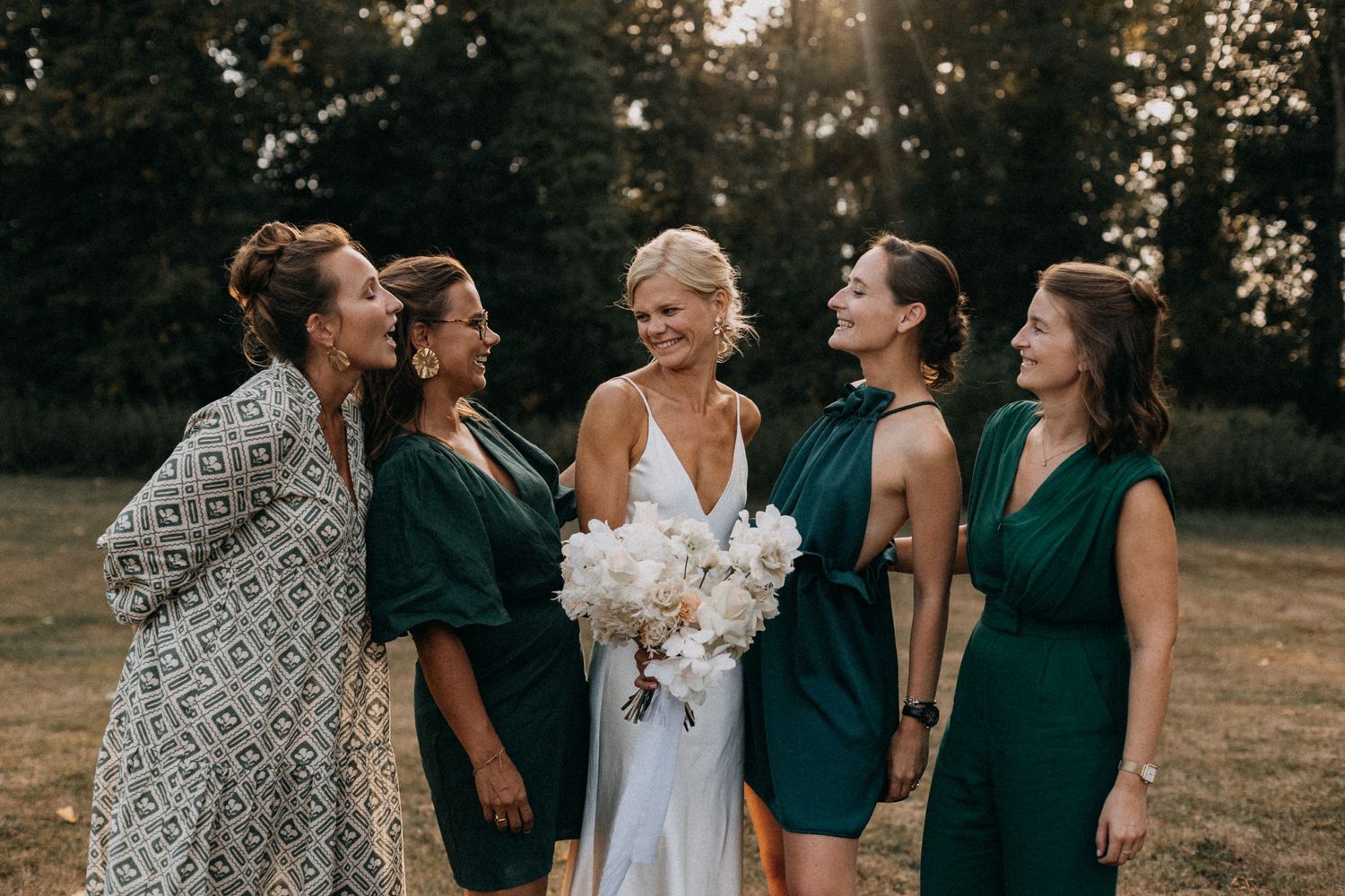 A bridal party shares joyful laughter during outdoor wedding photos at sunset.