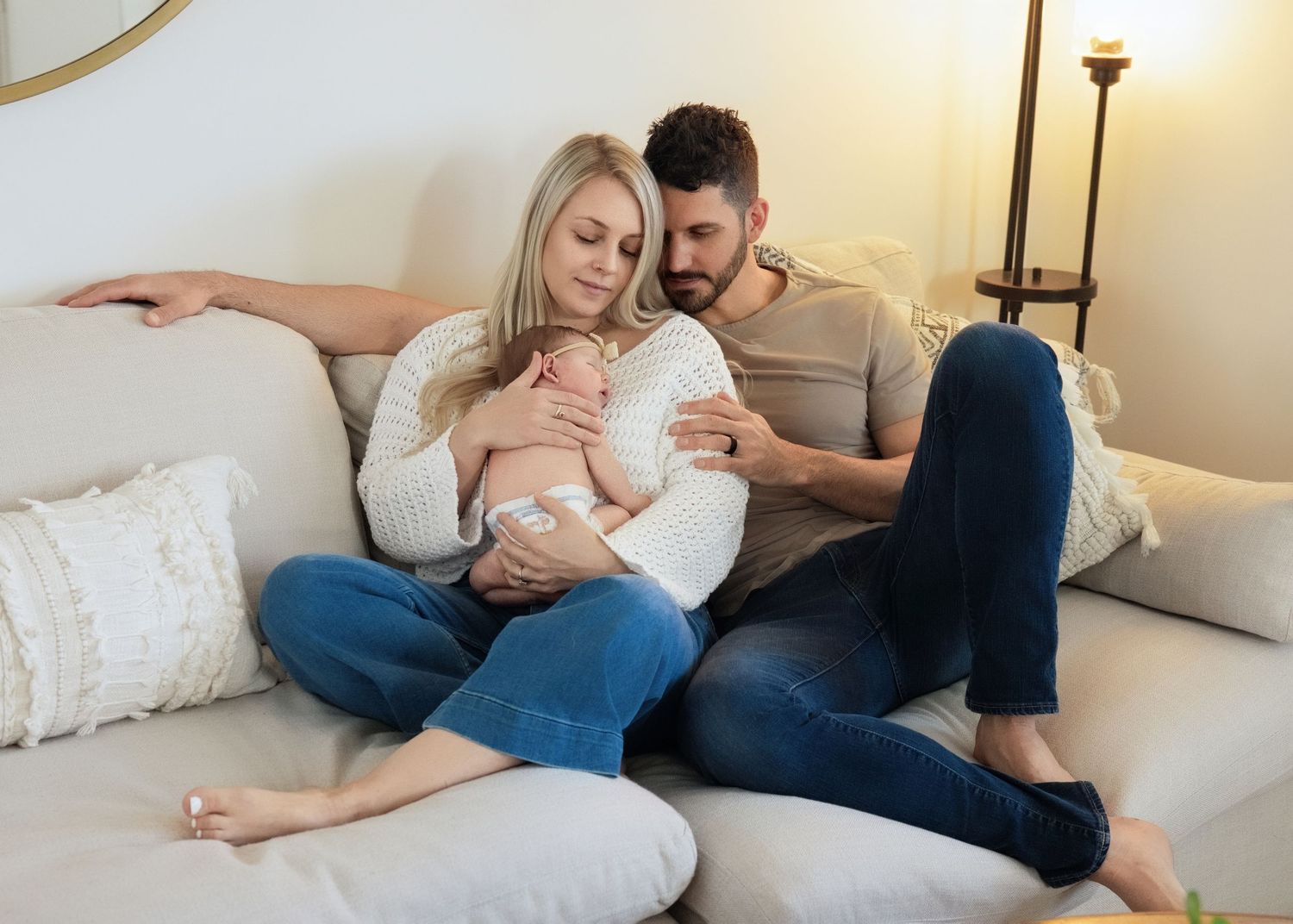 A couple relaxes together on their couch while cuddling their new baby intimately. In home newborn session salt lake city