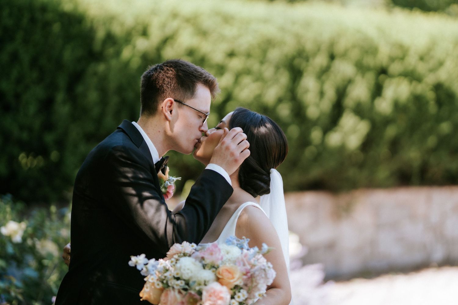 Couple shares tender moment during outdoor wedding ceremony with greenery in background.