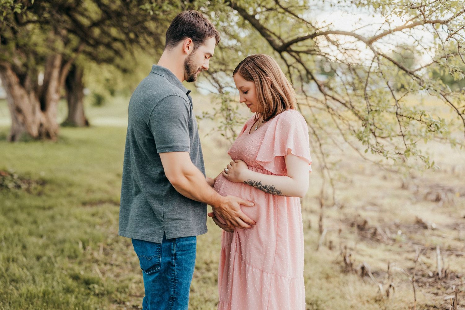 Spring maternity session showing couple in casual attire walking through grassy field.