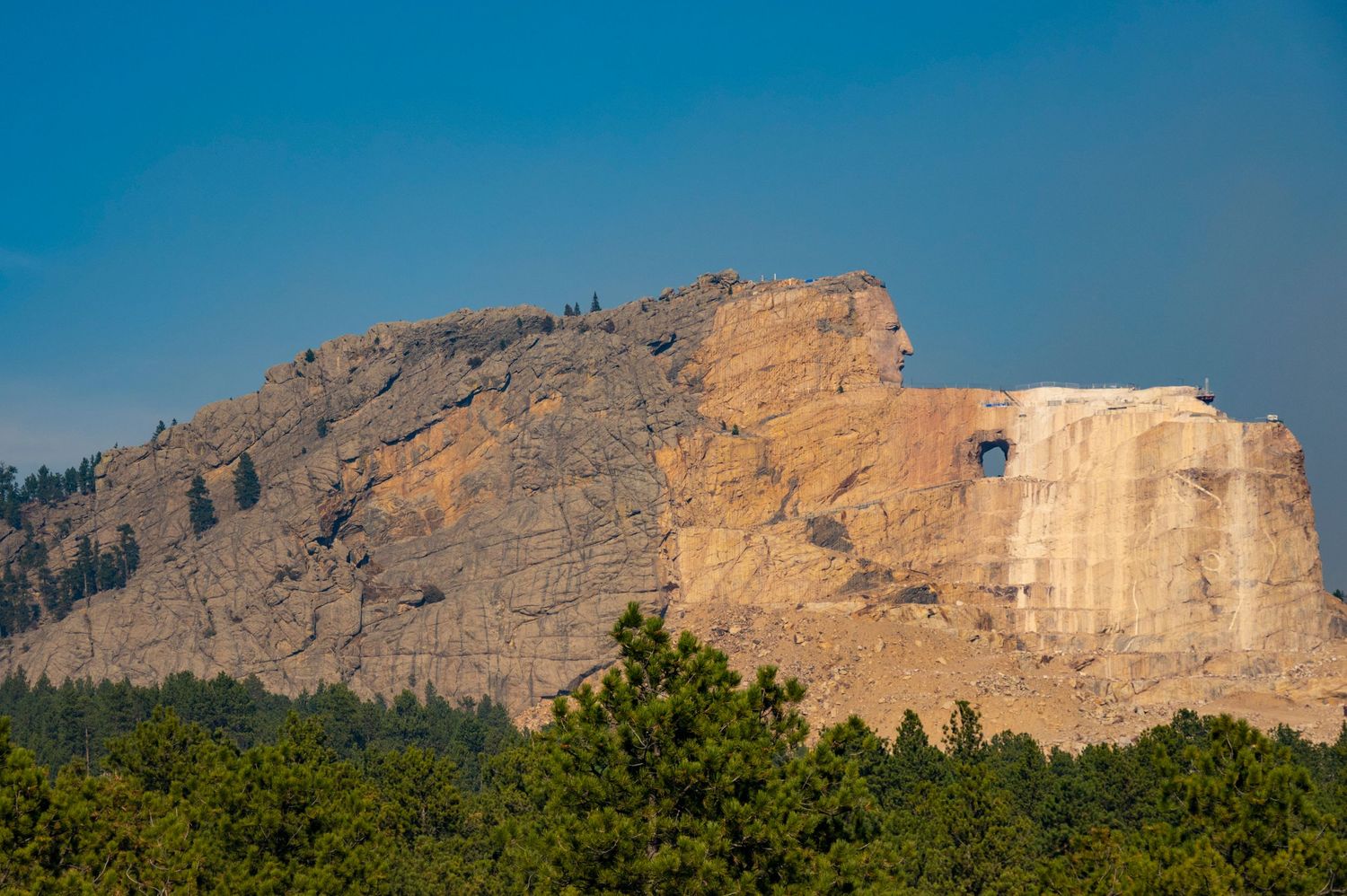 Carved face of Crazy Horse Memorial on mountain cliff under blue sky.